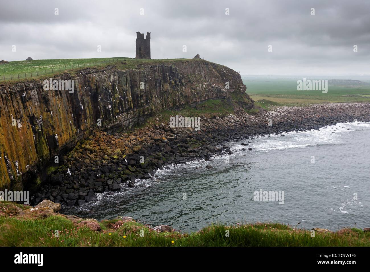 The Gull Crag cliffs and the ruined Lilburn Tower, Dunstanburgh Castle, Northumberland, England, UK, from Castle Point on an overcast, gloomy day Stock Photo