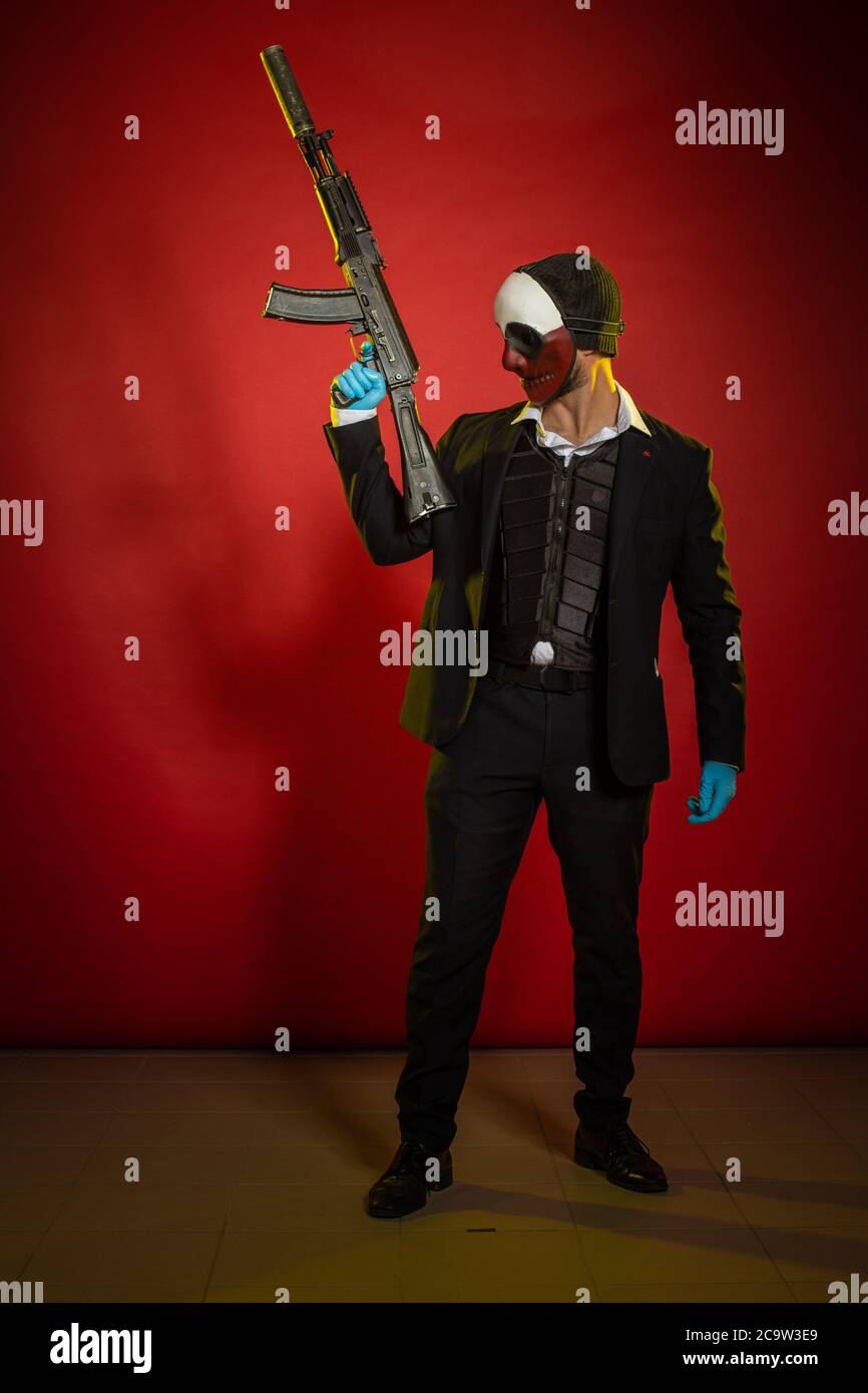 Actor man in a mask with a weapon in his hands posing on a red