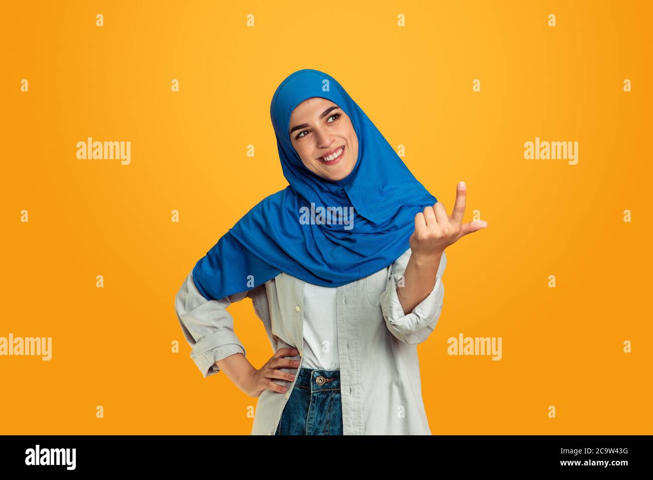 Pointing. Young muslim woman isolated on yellow studio background. Stylish, trendy and beautiful female model. Human emotions, facial expression, sales, ad, shopping concept. Copyspace. Stock Photo