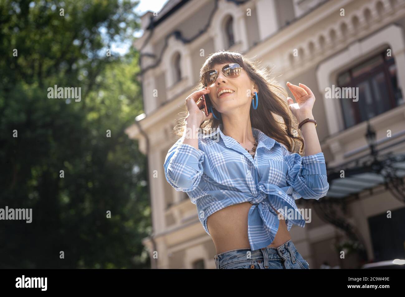 Joyful girl speaks on the phone in sunglasses. Portrait of a woman in  sunglasses. A young girl in a blue plaid shirt with glasses speaks on the  phone Stock Photo - Alamy