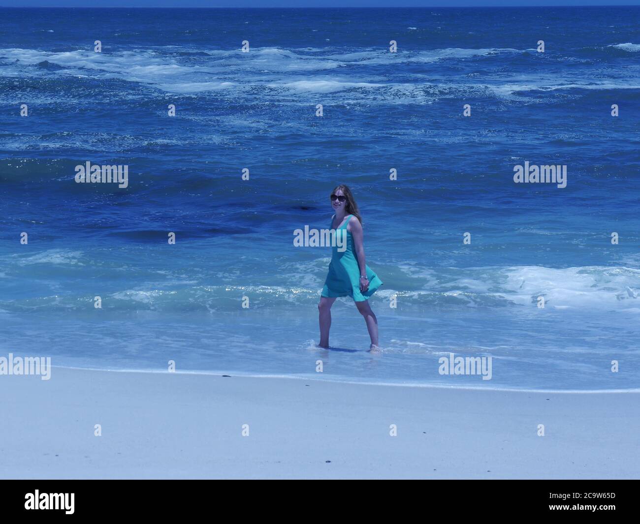 Pretty young woman in summer dress and sunglasses walks happily in sea Stock Photo