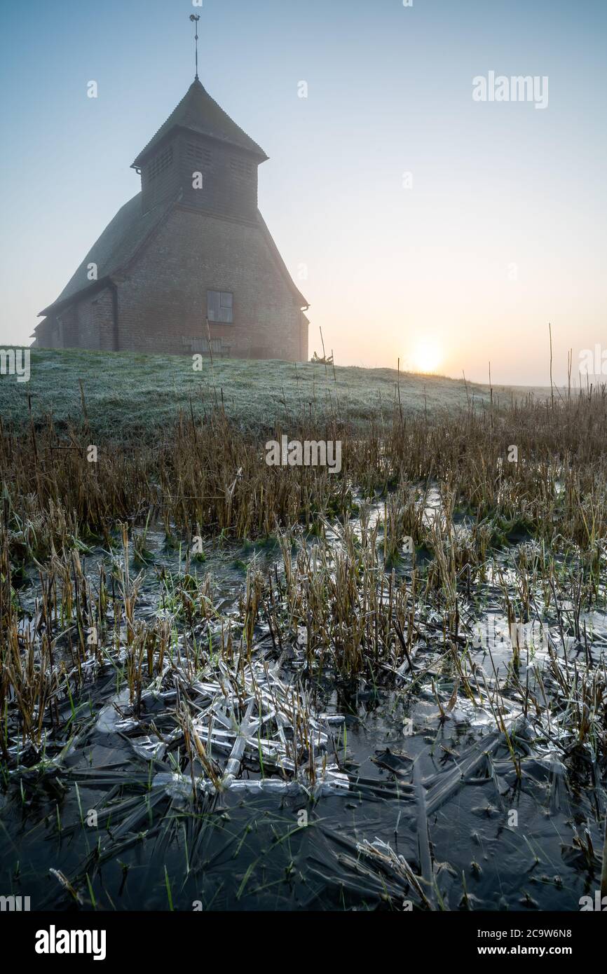 St Thomas à Becket Church in Fairfield at sunrise after the fog moved in. Low shot with ice formations in the drainage ditches. Stock Photo
