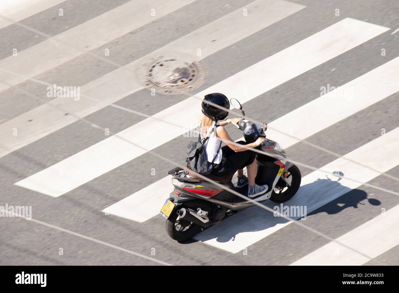 Belgrade, Serbia - July 30, 2020: Young woman riding a scooter vespa motorbike in empty city street pelican crossing, from above Stock Photo