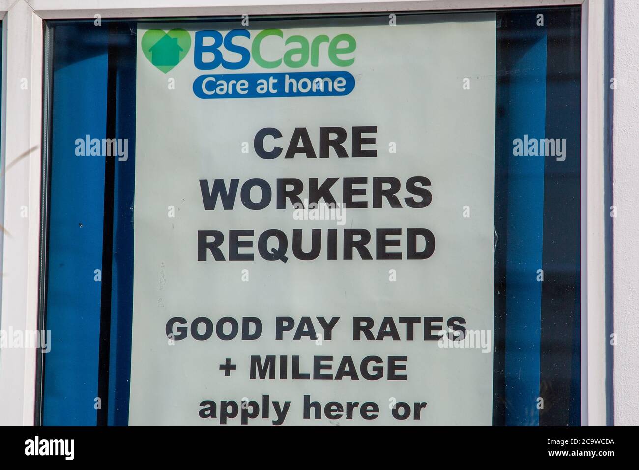a sign in the window of an employment agency stating care workers required and the rates of pay or wages Stock Photo