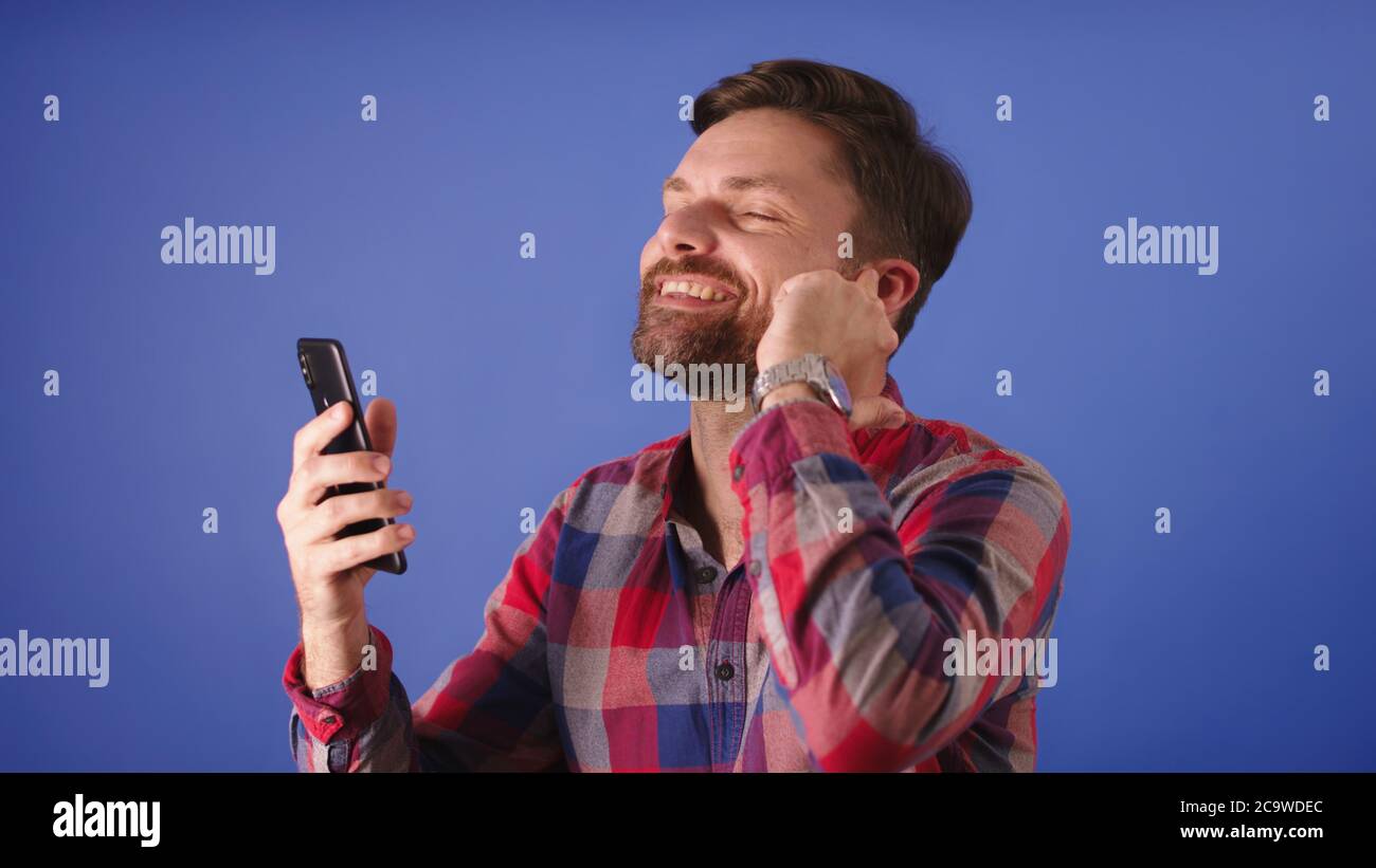 Attractive excited young bearded man having a conversation on the smartphone using the wireless headphones. High quality photo Stock Photo