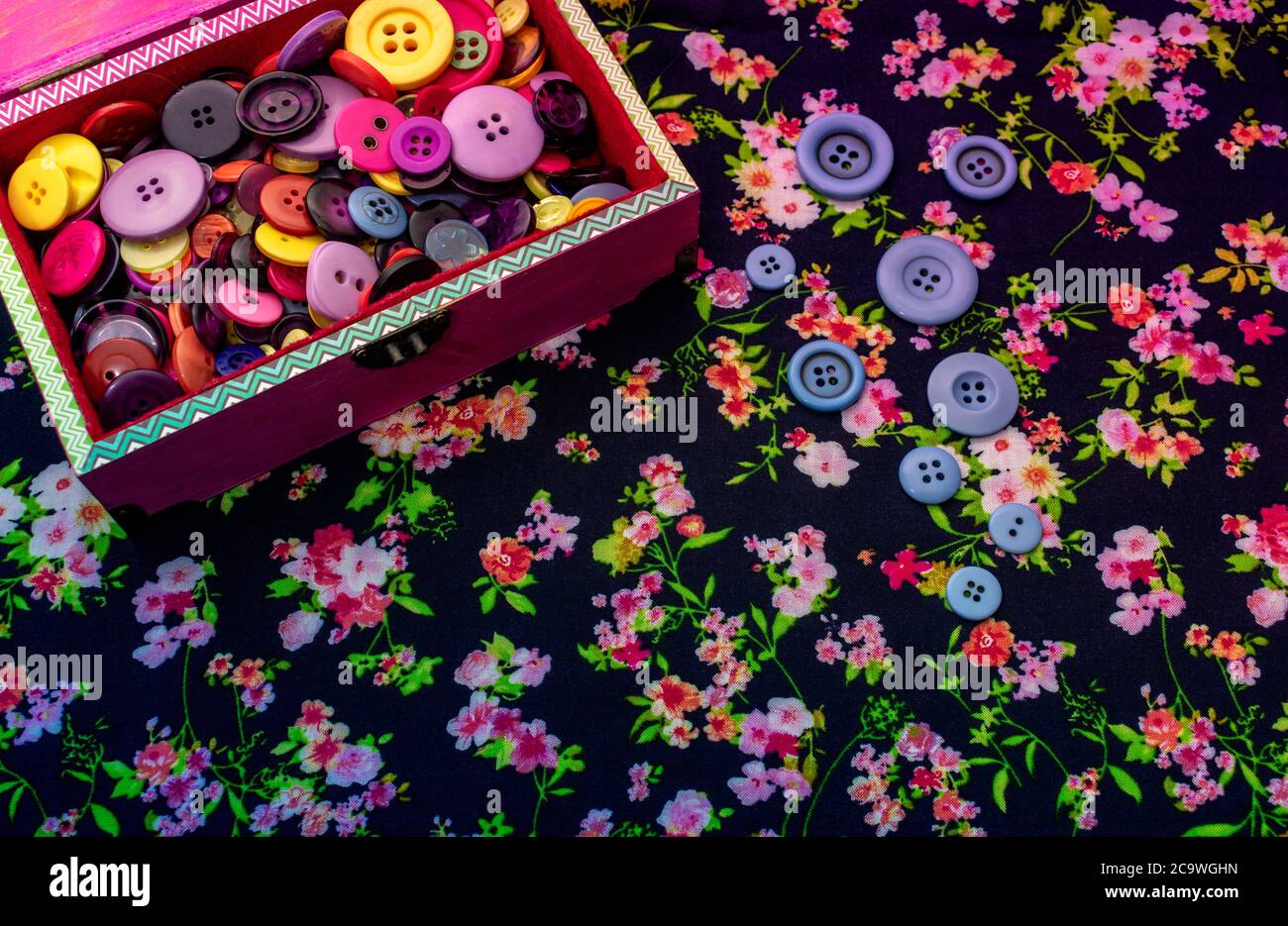 Colorful sewing button box over flowered fabric background with copy space Stock Photo