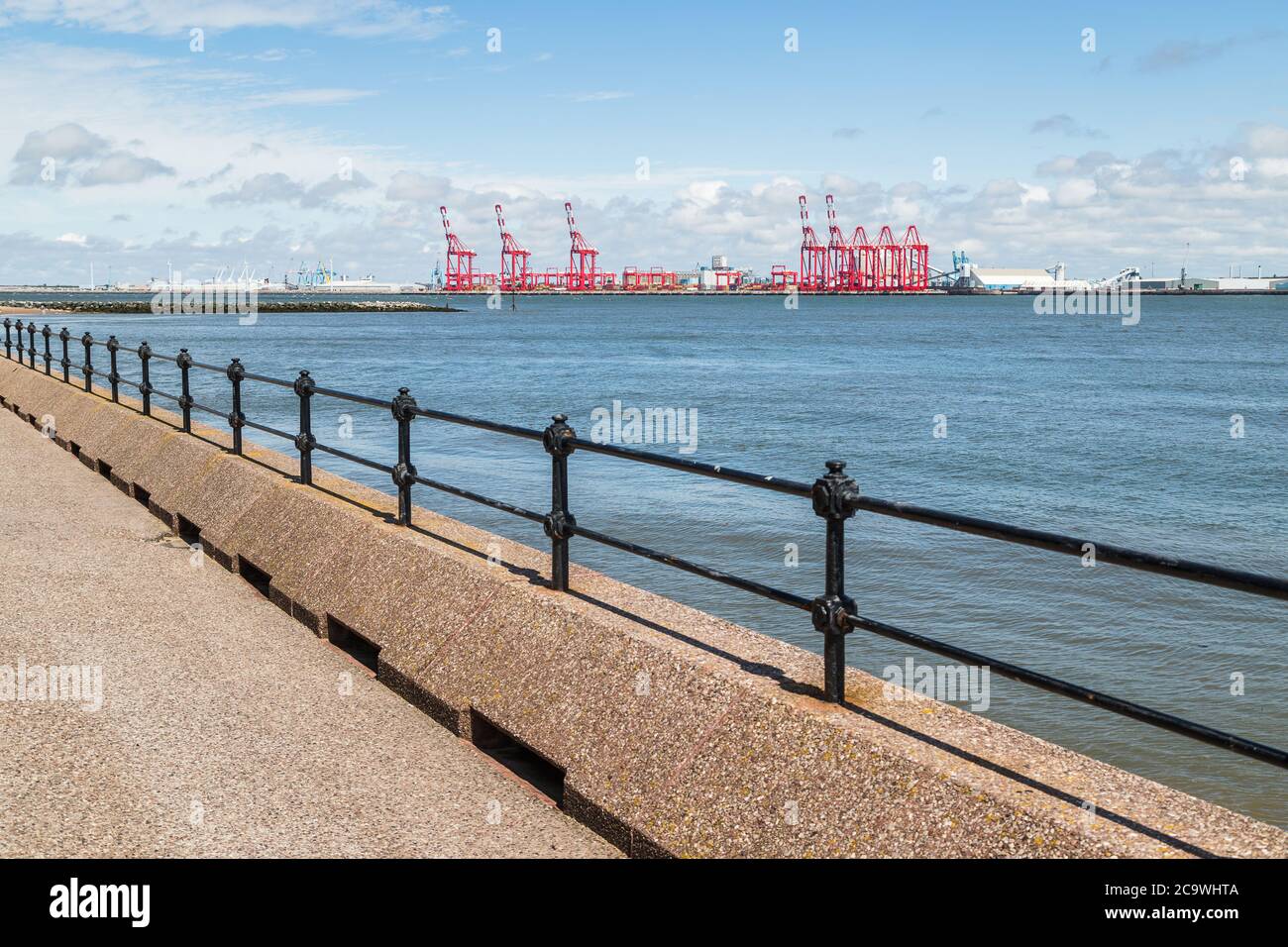 Overlooking the railings on the promenade at New Brighton near Liverpool towards the large red cranes at Seafort dock. Stock Photo