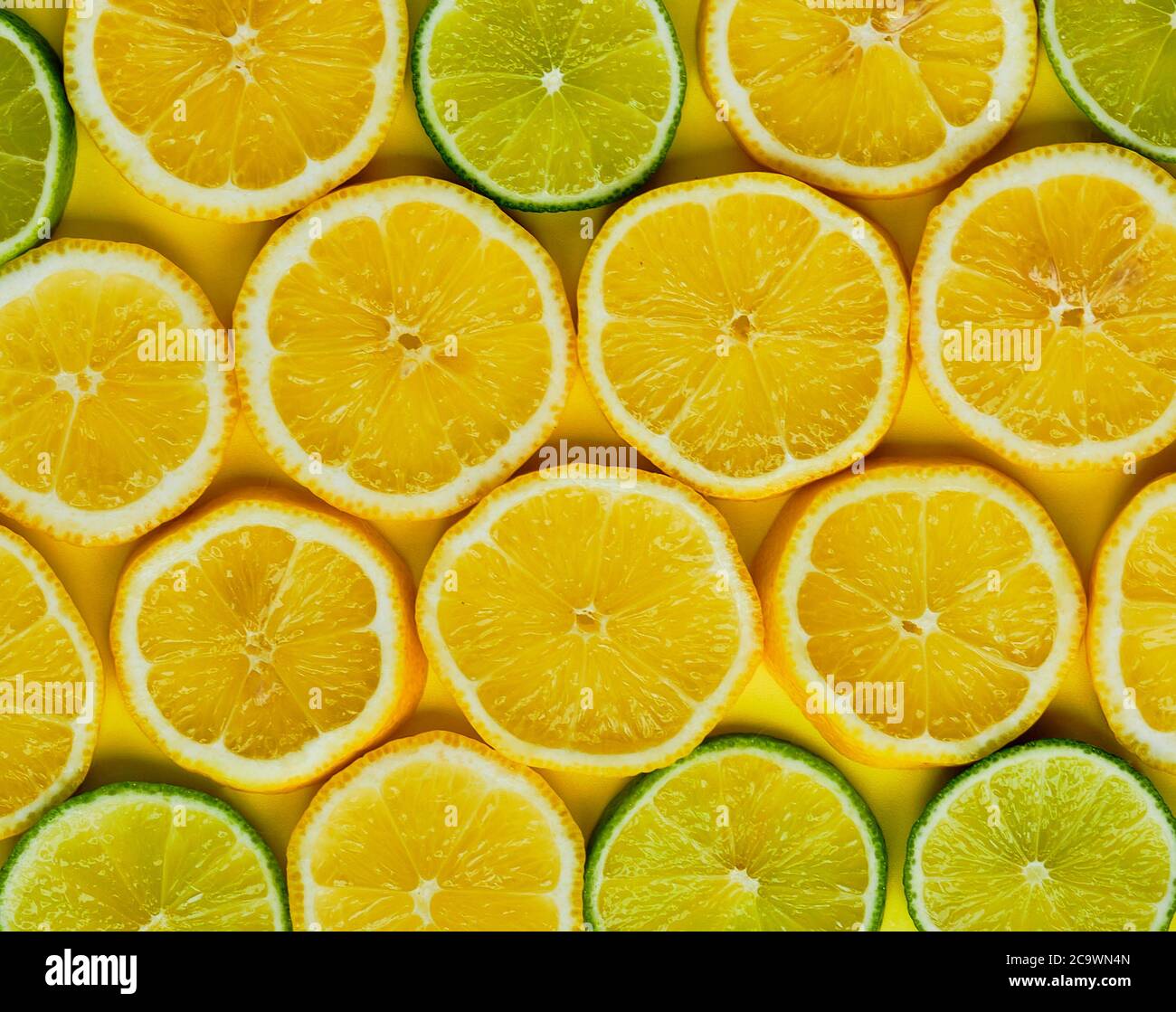 Sliced lemons and limes in round slices on yellow background. Top view Stock Photo