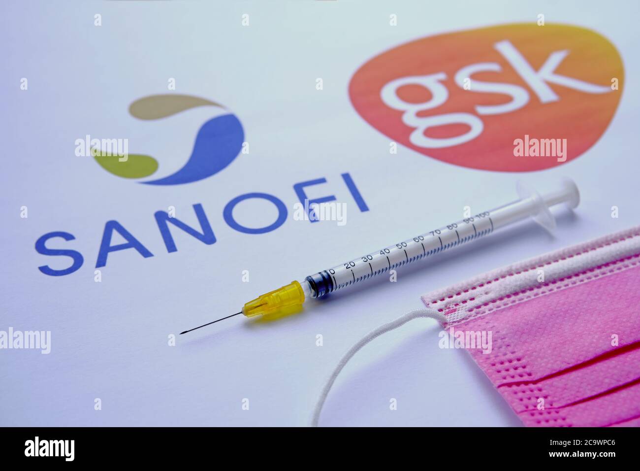 Stone / UK - August 2 2020: SANOFI GSK logos on a blurred background and syringe with a viral mask on front. Concept for COVID-19 vaccine. Selective f Stock Photo