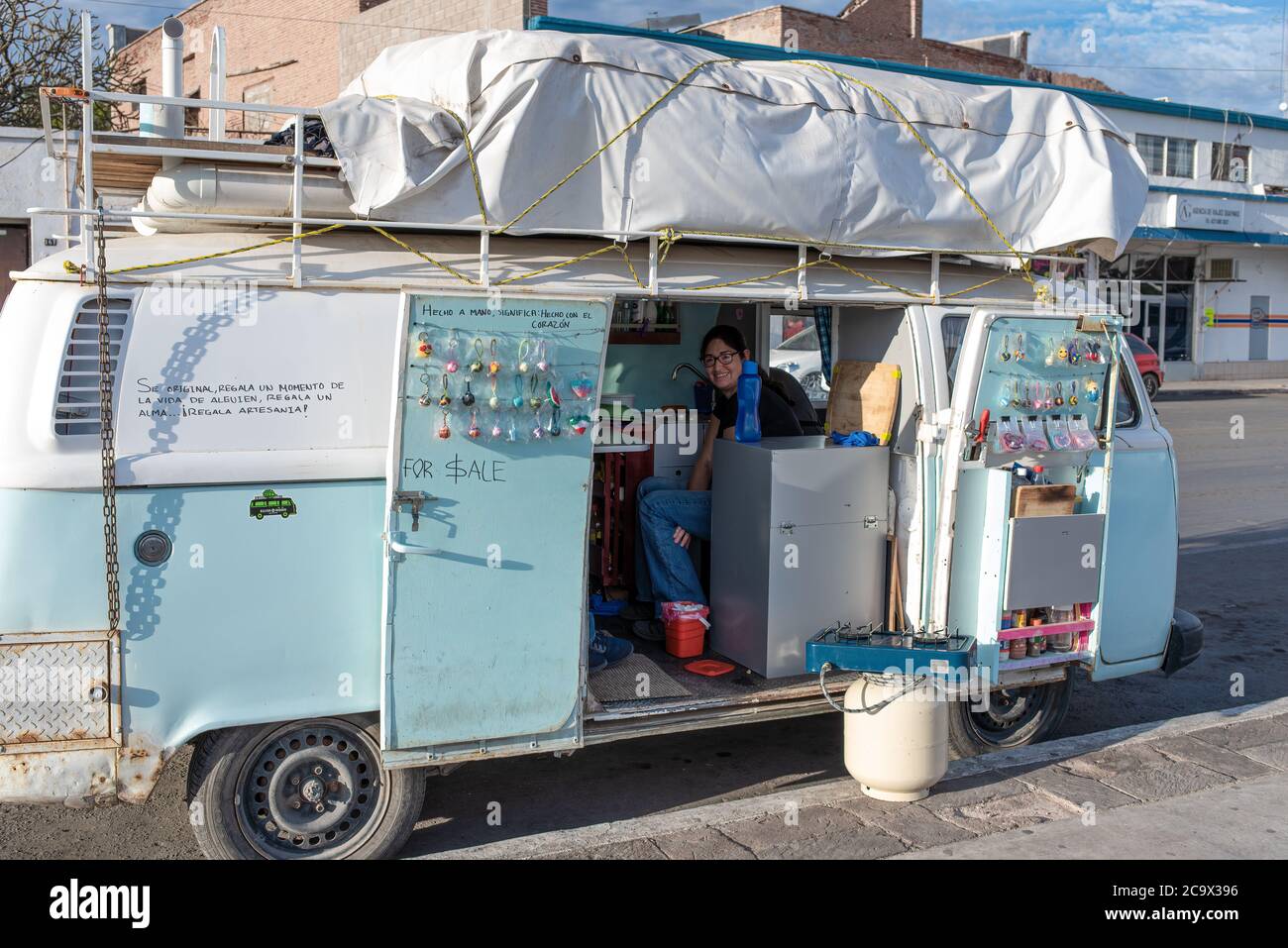 A young woman sells jewelry from her VW van parked along the street in downtown Guaymas, Sonora, Mexico. Stock Photo
