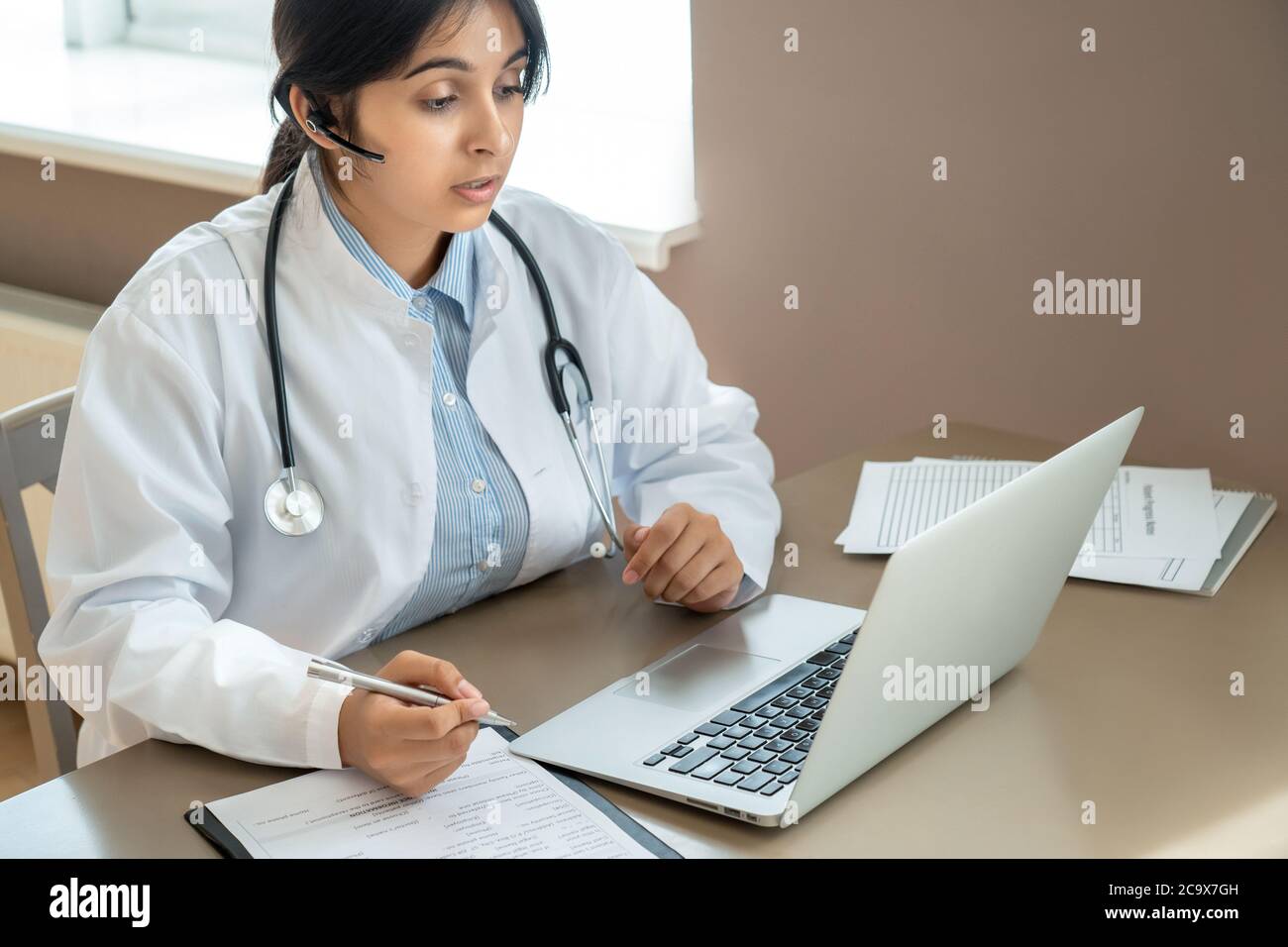 Indian telemedicine doctor wear headset talking to patient by online video call. Stock Photo