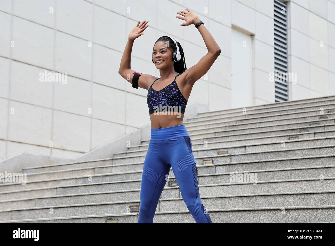 Smiling fit pretty young Black woman doing jumping jacks exercise to warm up before training Stock Photo