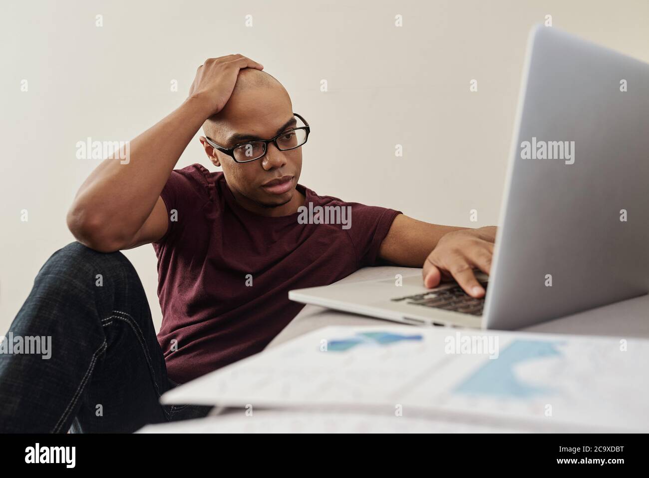 Pensive young African-American businessman in casual clothes analyzing financial report on laptop screen Stock Photo