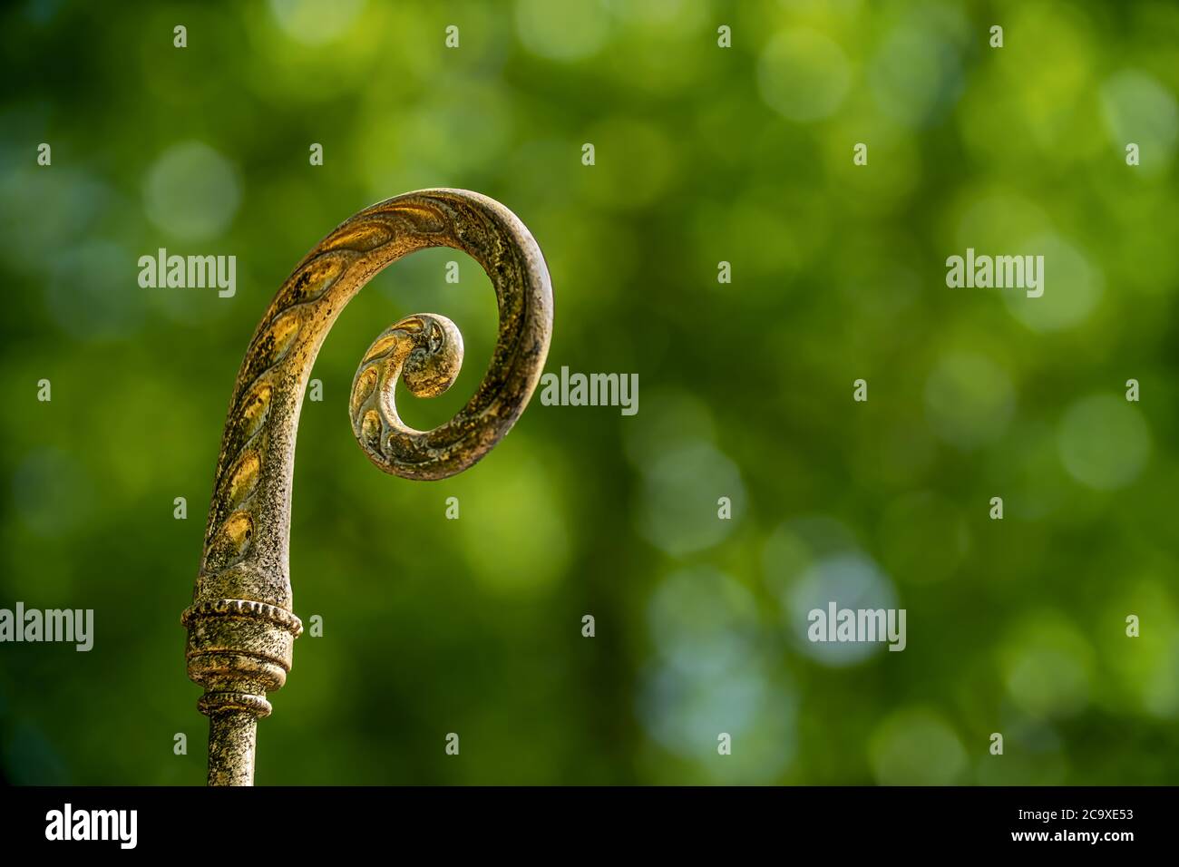 gilded bishop's staff of a statue isolated on blurry green background Stock Photo