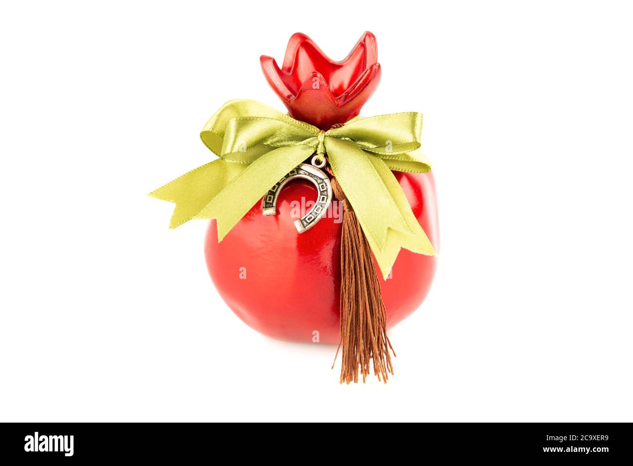 Red pomegranate souvenir with green ribbon, tassel  and horseshoe isolated on white background. Stock Photo