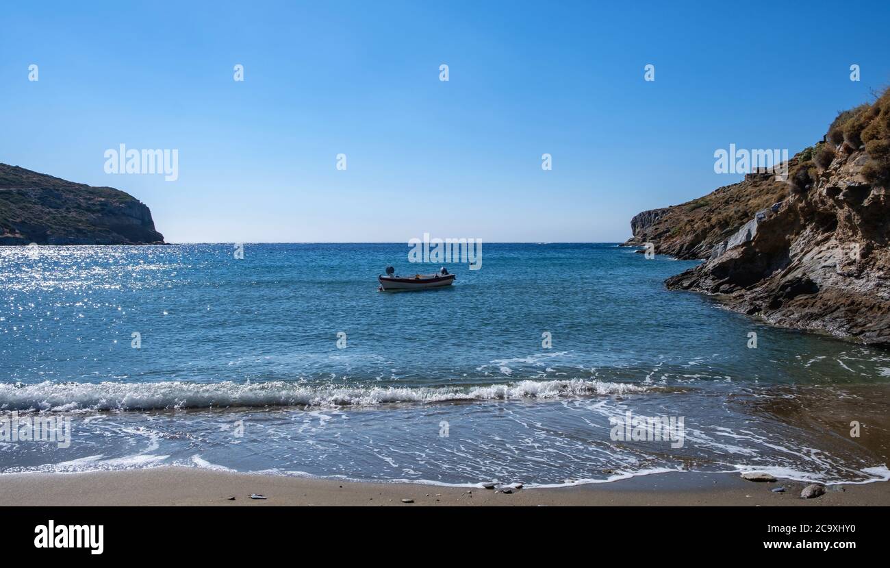 Small boat on the sea, reflections on calm sea water, blue clear sky background, Spathi sandy beach. Greece. Kea island. Stock Photo