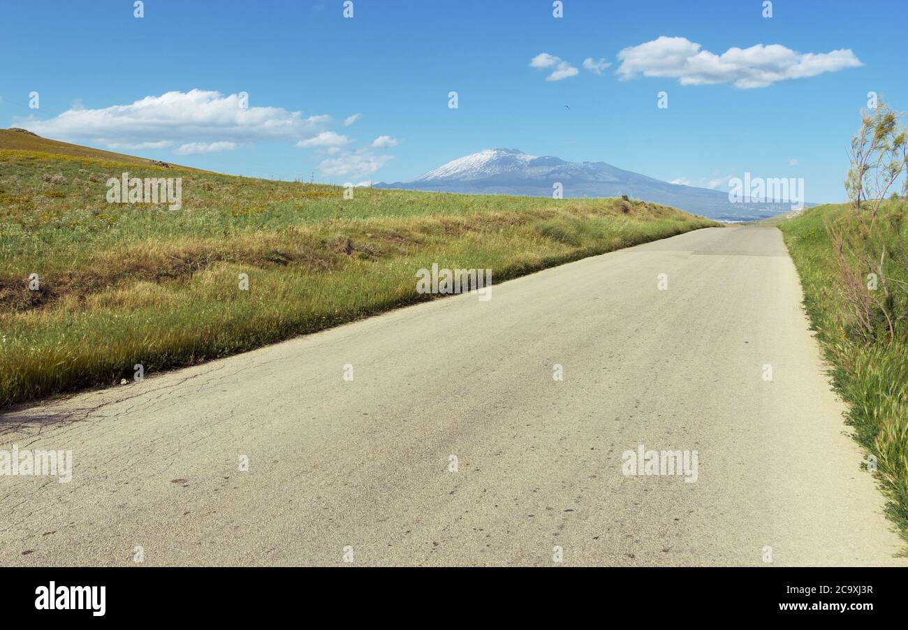 landscape of a Sicily rural road and the Etna Mount below white clouds Stock Photo