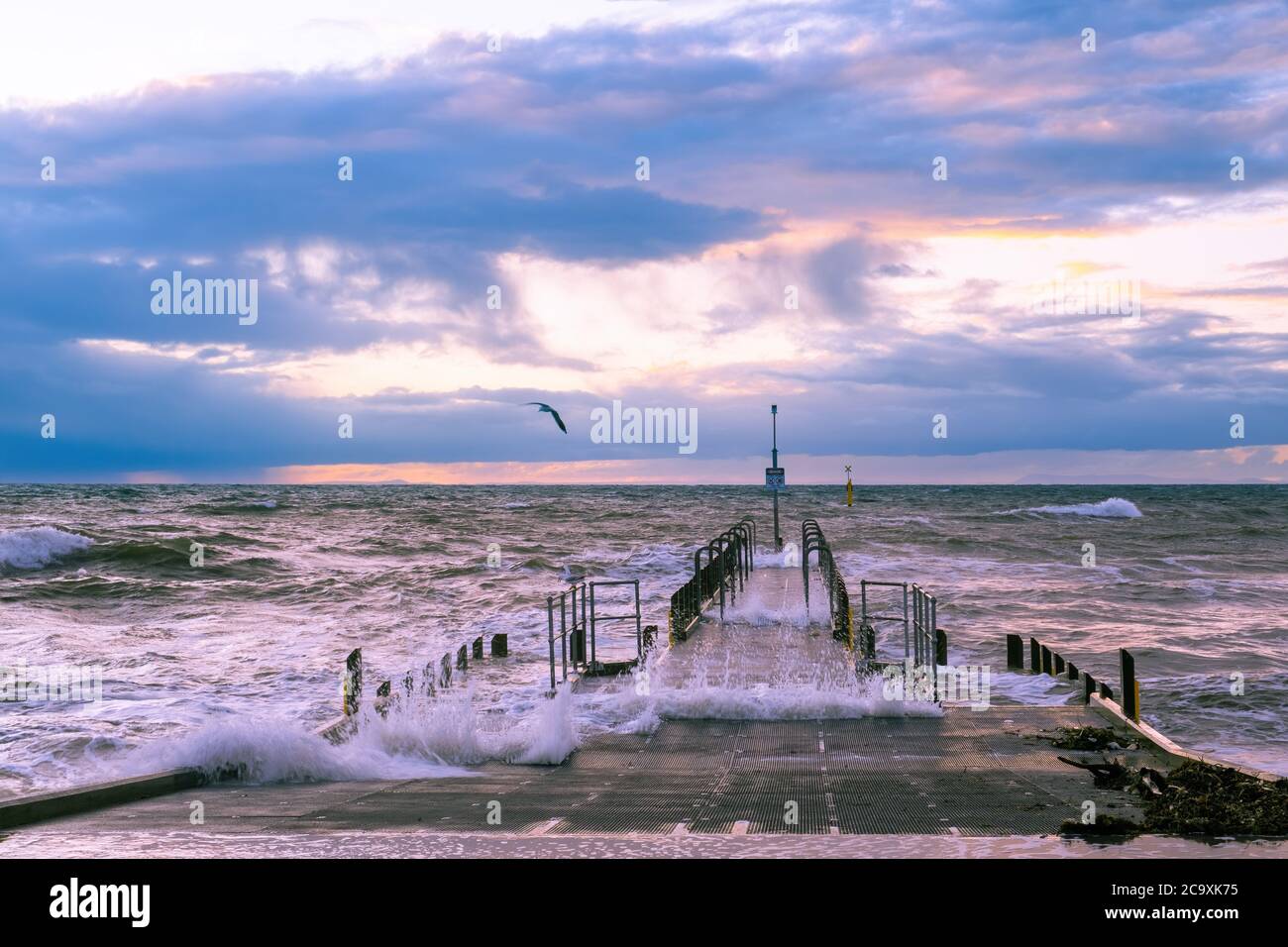 Beautiful sunset over foreshore with big waves and boat jetty Stock Photo
