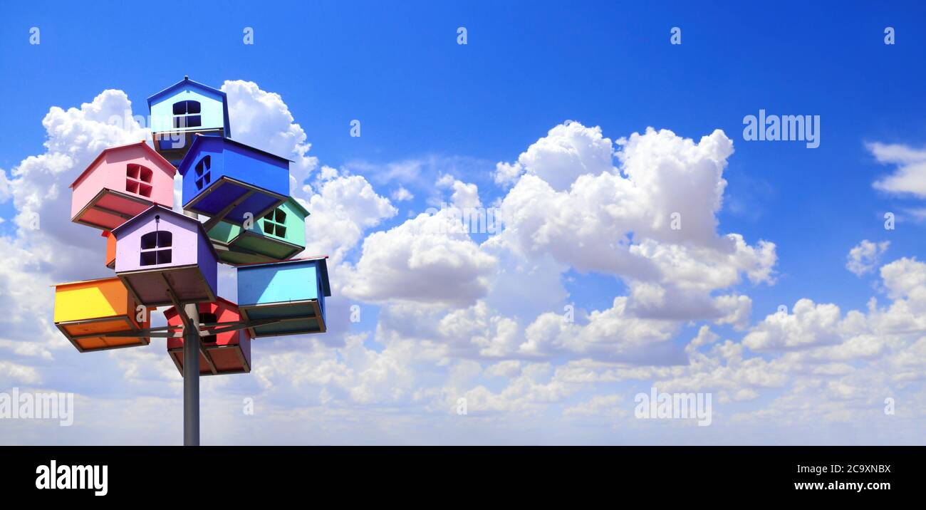 Horizontal banner with colorful nesting boxes on blue sky background. Many birdhouses of different colors and blue sky with clouds Stock Photo