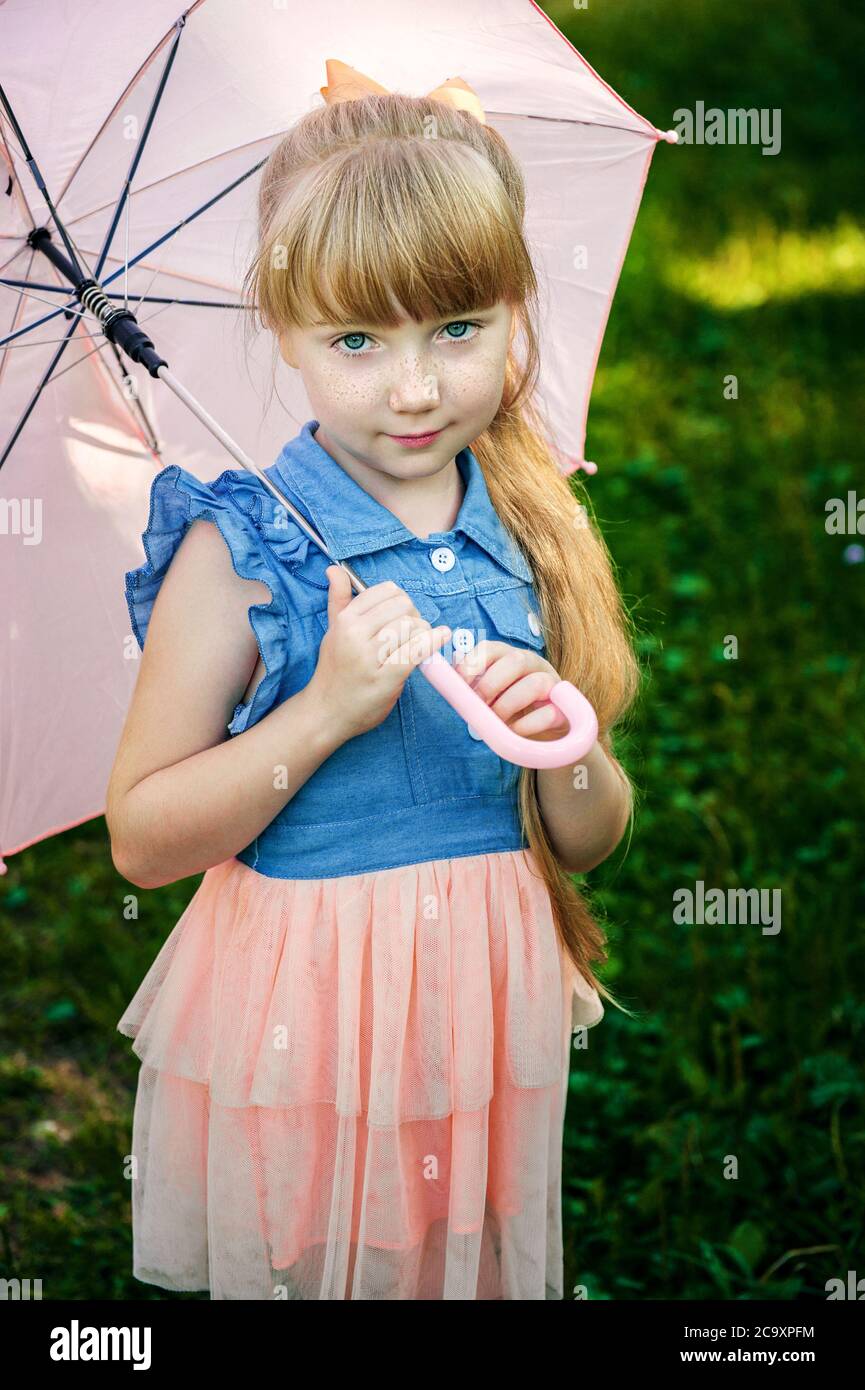 charming red-haired girl with a long braid and a pink umbrella is smiling. Girl with an umbrella in the garden Stock Photo
