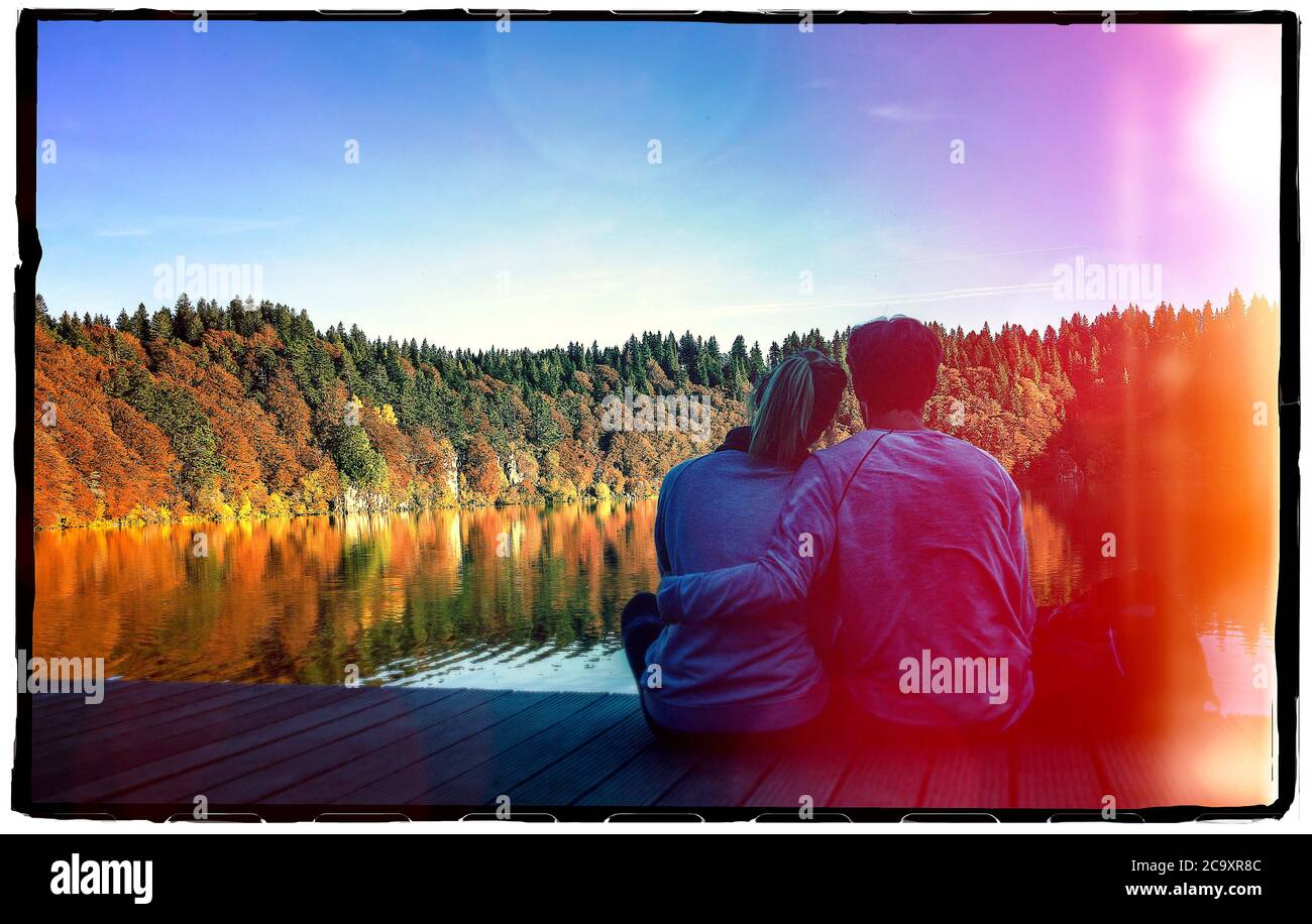 Couple sitting at Lake Pavin, volcanic lake, Auvergne Volcanoes Natural Park, Puy de Dome, France Stock Photo