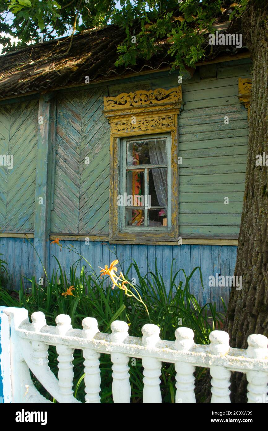 Traditional ornamented yellow open shutters of an old wooden rural house in the village of Belarus. Old shabby teal house Stock Photo