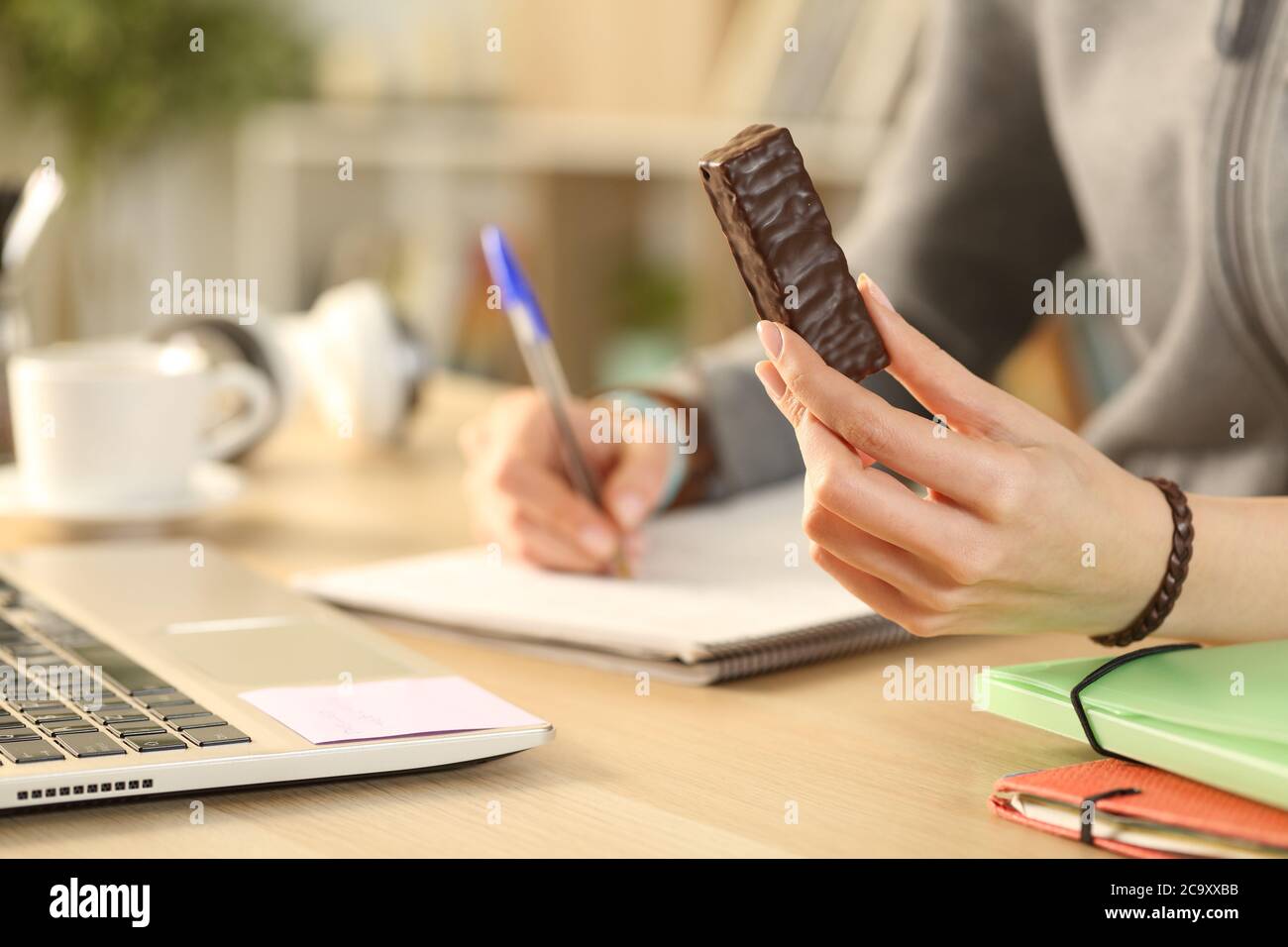 Close up of student girl hands holding chocolate snack bar studying at home Stock Photo