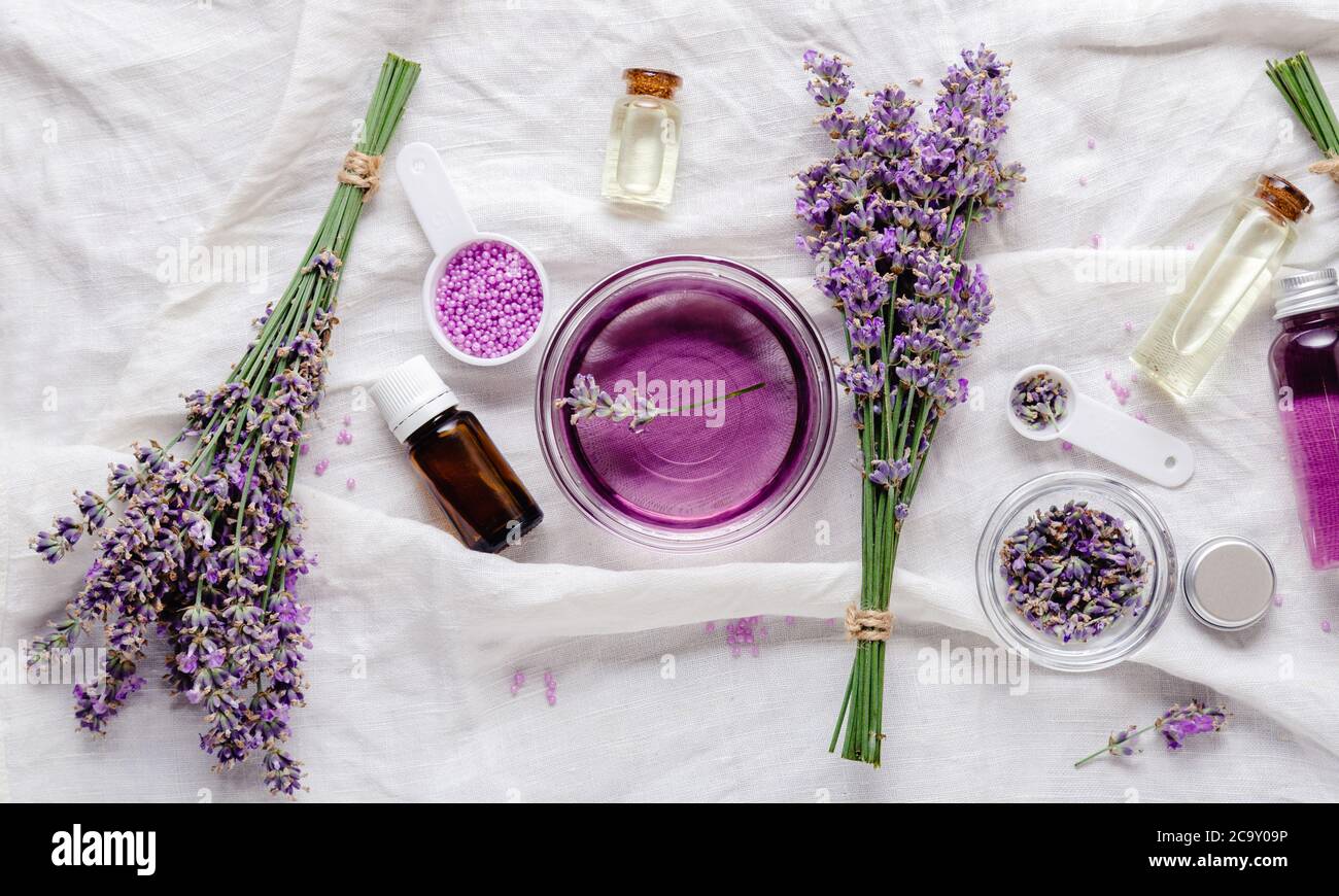Lavender oils, liquids, parfumes, lavender flowers on white fabric. Set skincare spa beauty cosmetic products. Lavender essential oil. Apothecary Stock Photo