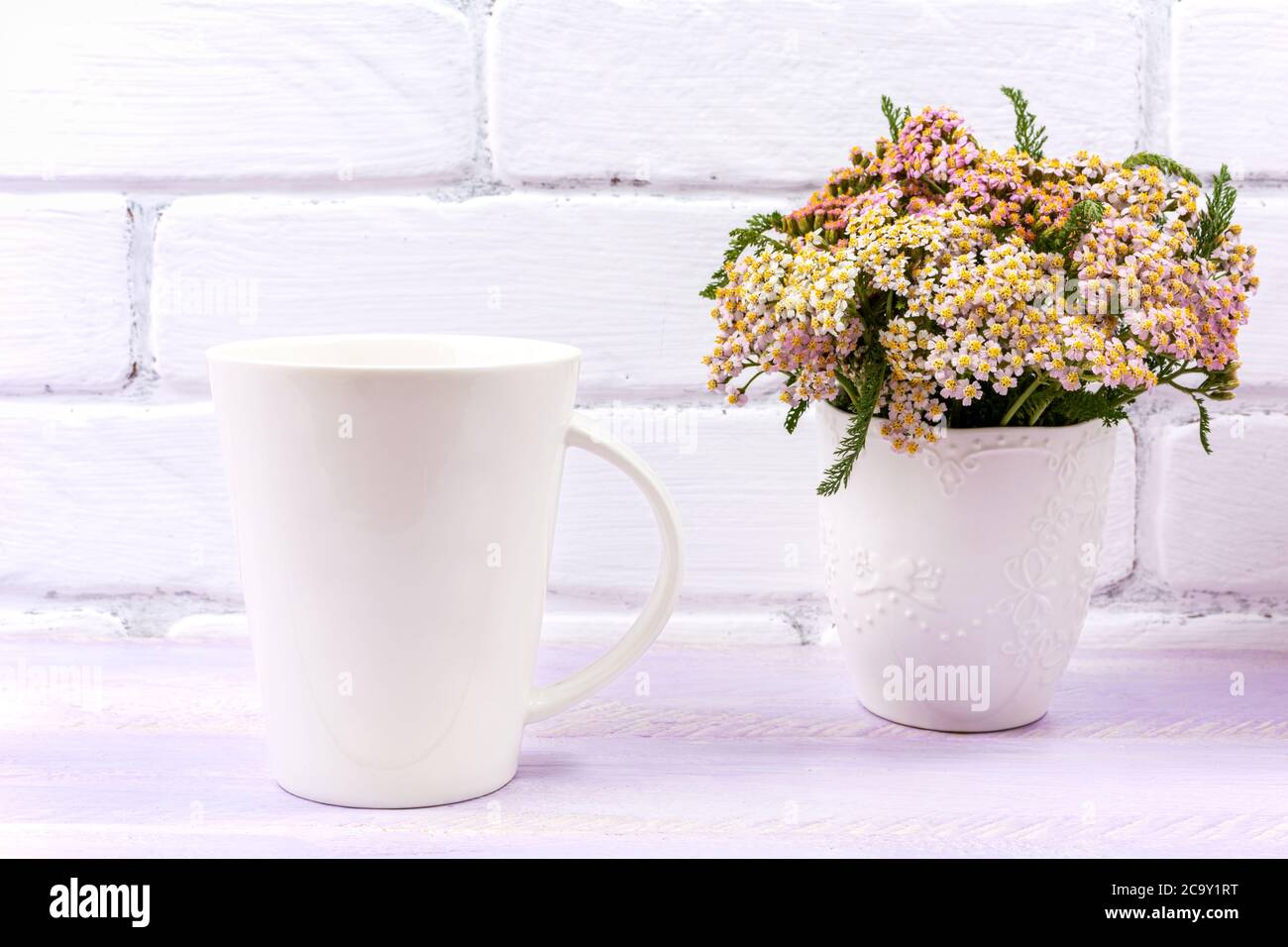 White coffee latte mug mockup with pink yarrow in the decorated vase.  Empty mug mock up for design promotion. Stock Photo