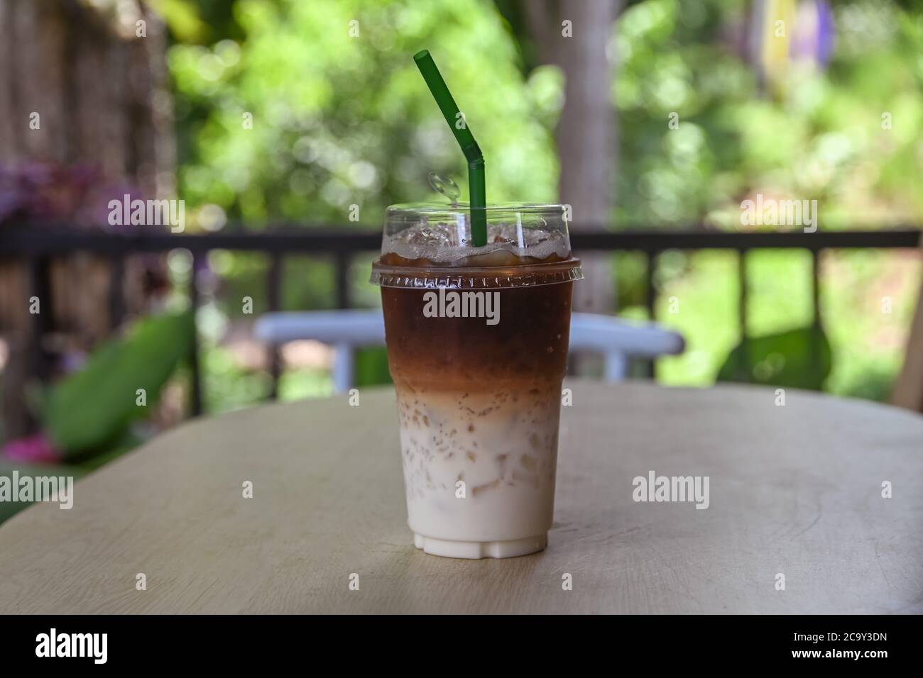 iced coffee in plastic cup for take away on wooden bar with green nature in garden Stock Photo