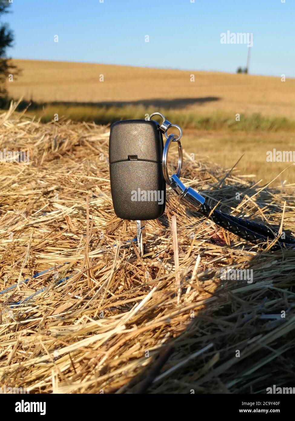 A car key placed in a hay bale with a beautiful view of the cultivated field. Stock Photo