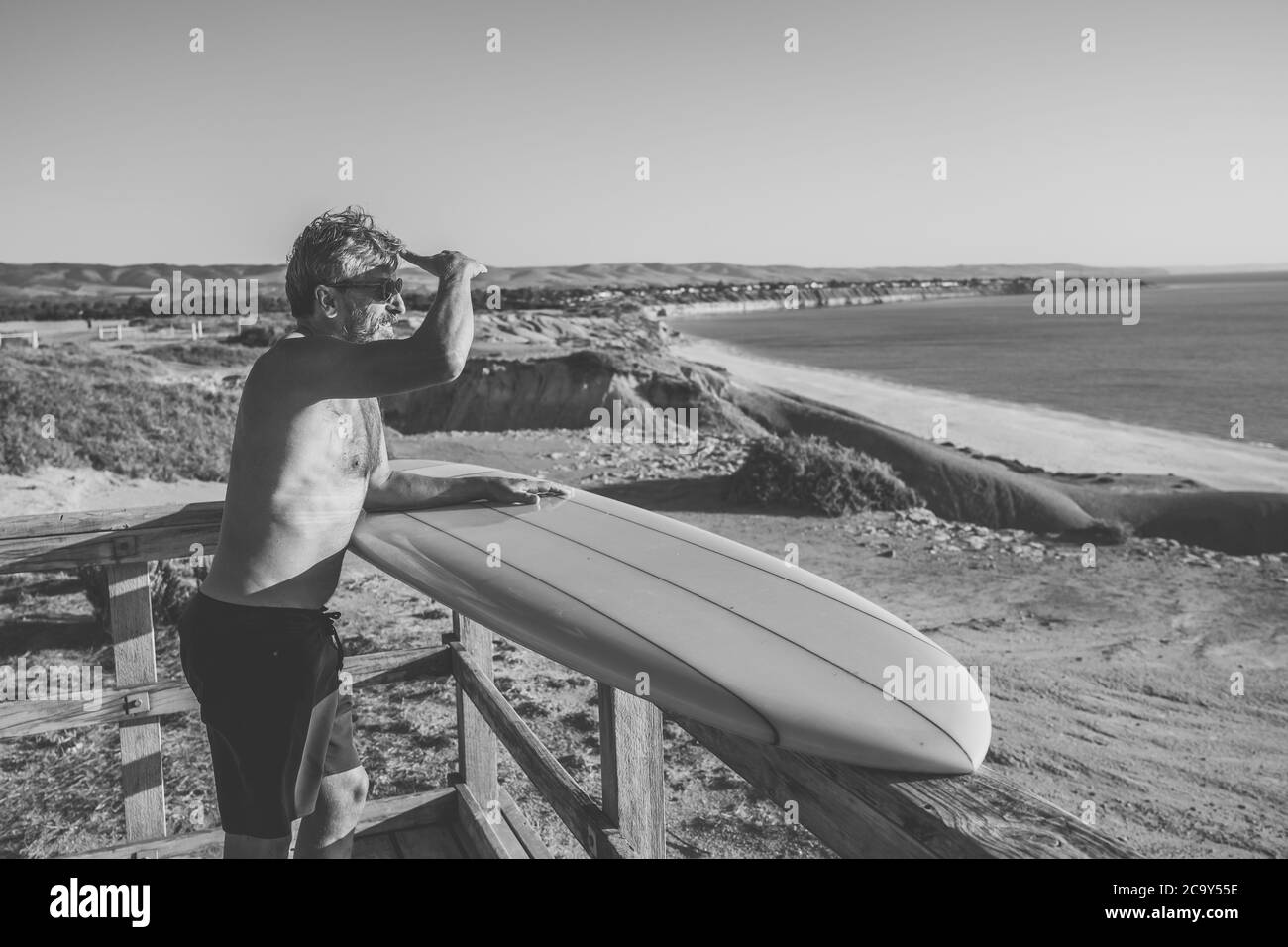 Attractive Australian mature man surfer with cool vintage surfboard on beach at sunset. Senior adult happy to be Back to surf . Outdoors sports advent Stock Photo