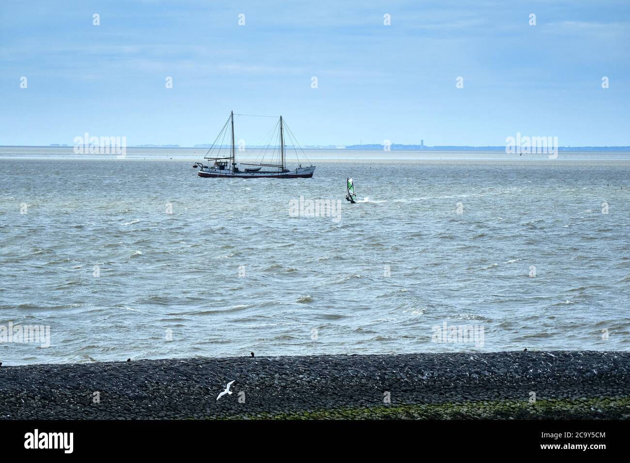 Harlingen,the Netherlands,July 23,2020:Wadden sea with windsurfer and old traditional sailing ship, black stone dike, pier and on the horizon the Stock Photo