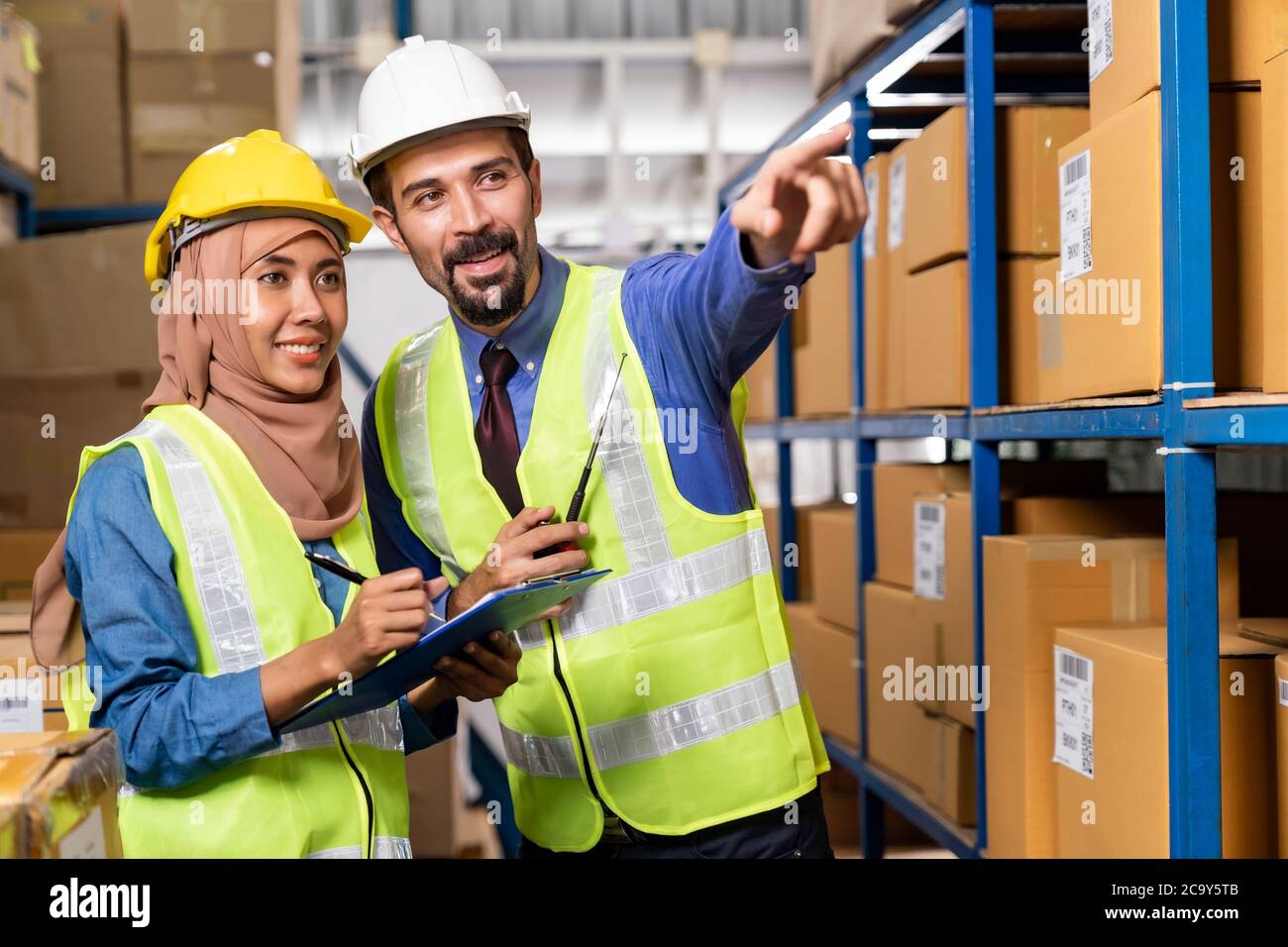 White caucasian warehouse manager command and assign job to muslim asian warehouse worker in distribution center. For business warehouse inventory and Stock Photo