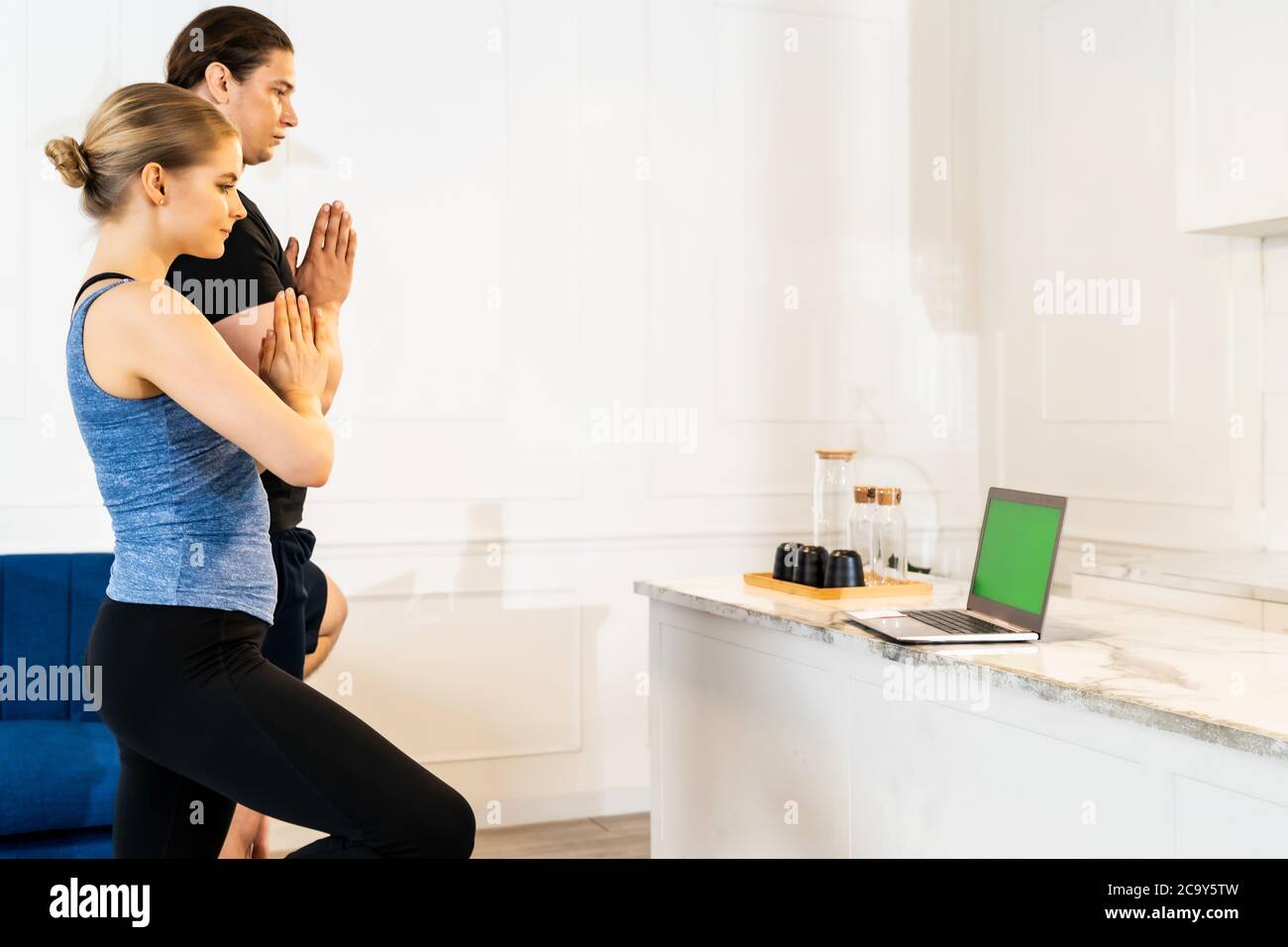 White caucasian fit sporty couple doing yoga tree pose in living room at home watching online tutorials from trainer on laptop. Working out, fitness s Stock Photo