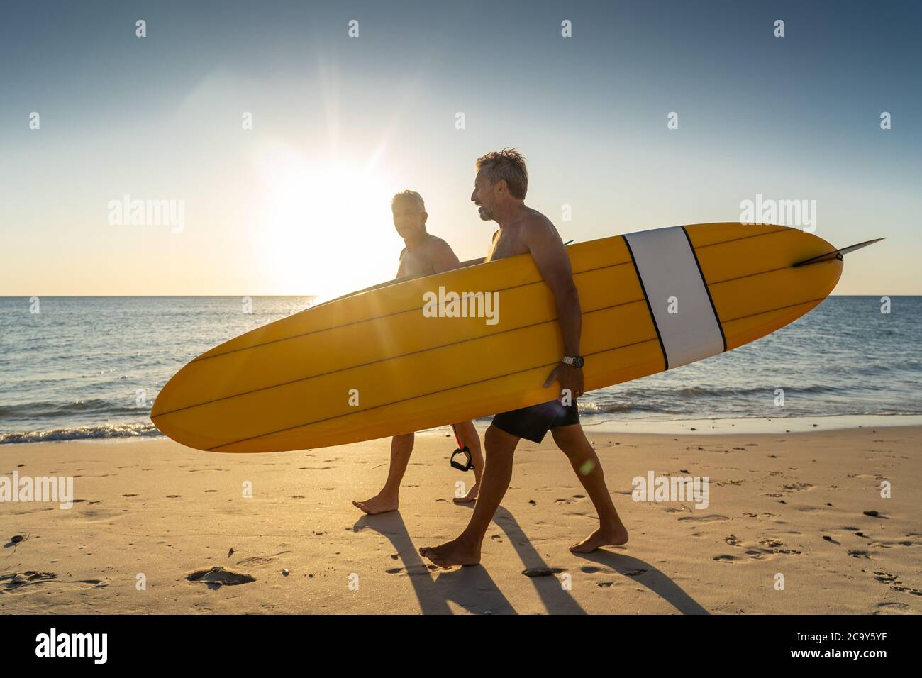 Two mature men walking with surfboards on beautiful beach enjoying paradise and retirement lifestyle. Attractive fit senior adults friends having fun Stock Photo