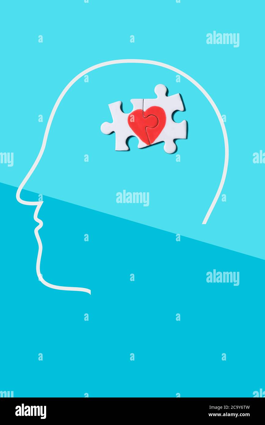 two pieces of a puzzle forming a heart in the silhouette of a mans head, on a background of two shades of blue Stock Photo