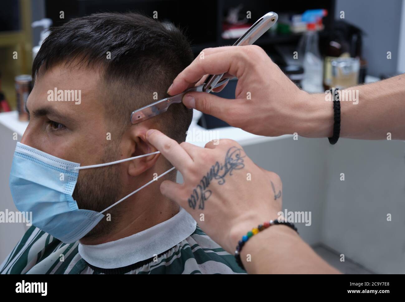 hairdresser's hands with tattoos cutting hair with a razor and client's