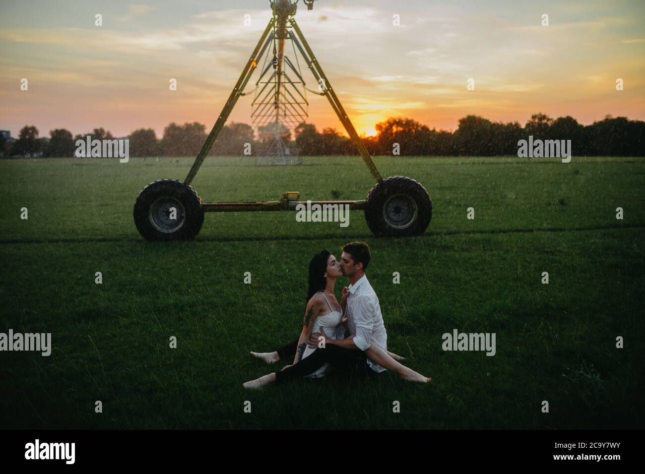 Drenched couple in love kisses and embraces among lawn under water ...