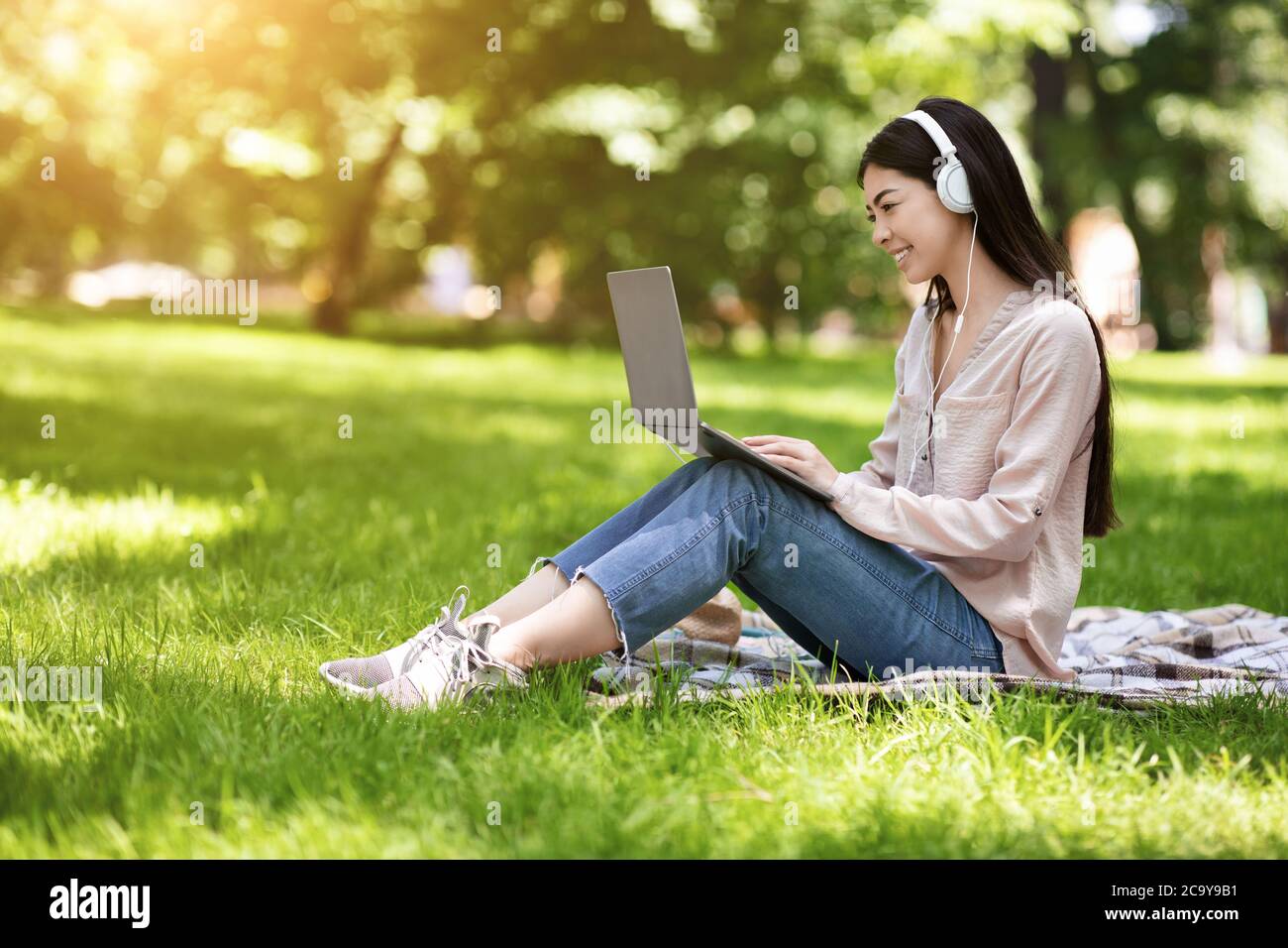 Happy Asian Girl Freelancer Working On Laptop In Park And Listening Music Stock Photo
