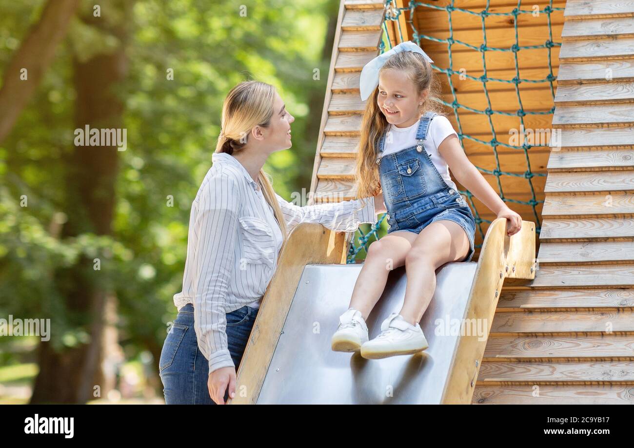 Little Girl Riding Slide Playing With Babysitter On Playground Outdoor
