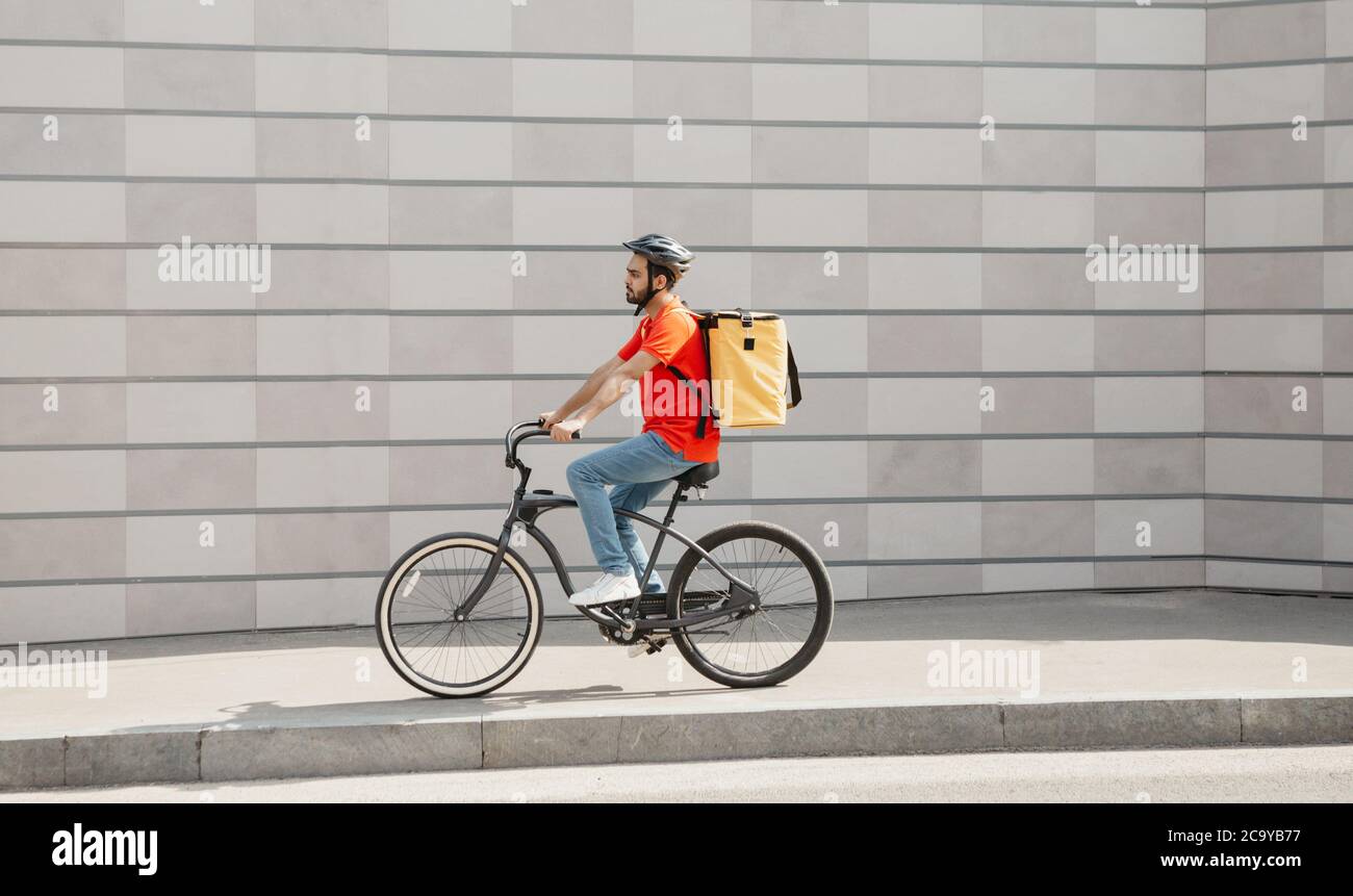 Road to client. Young man in helmet with backpack goes on bicycle Stock Photo
