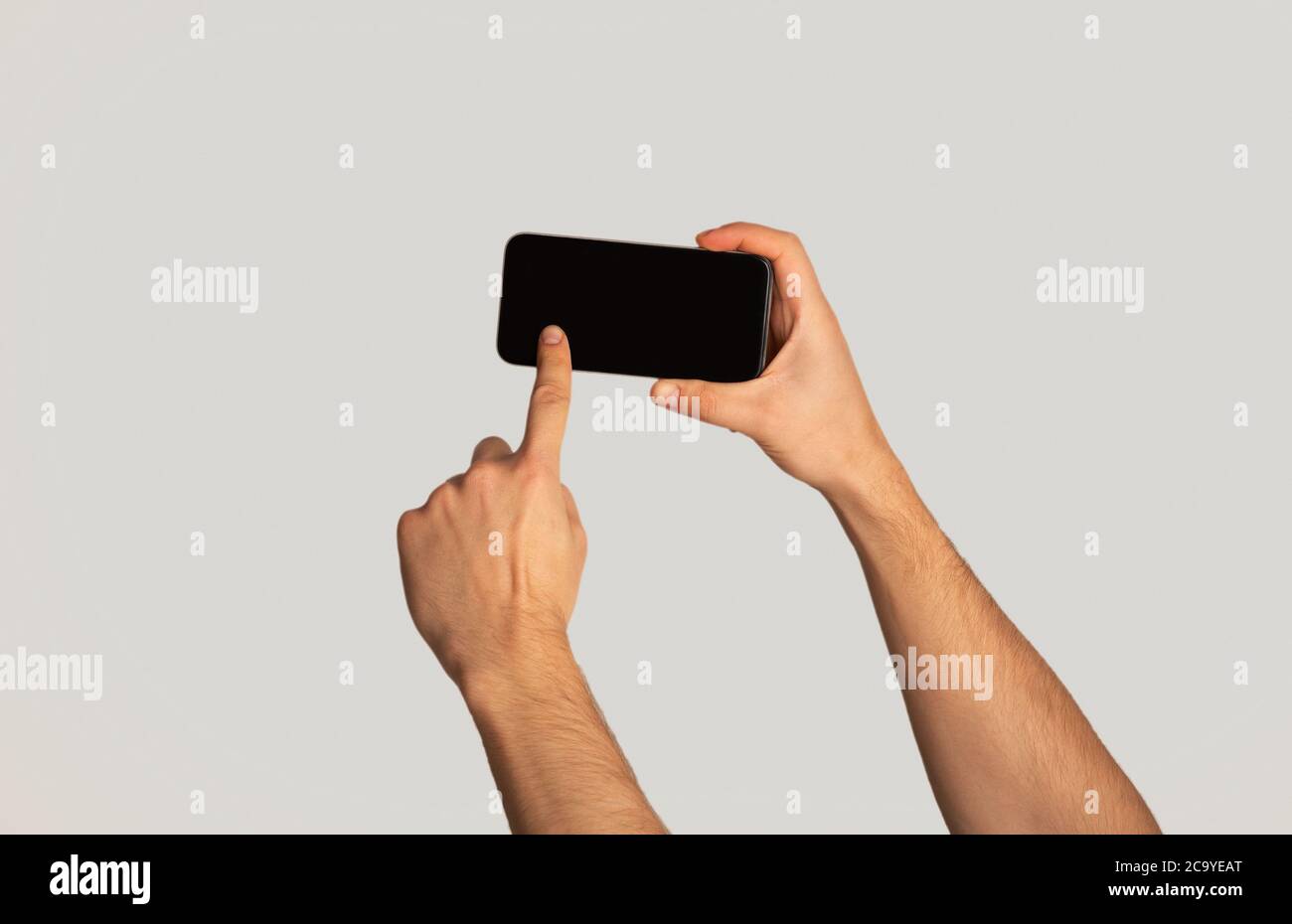Unrecognizable millennial man touching screen of cellphone over light background, space for mobile app design Stock Photo