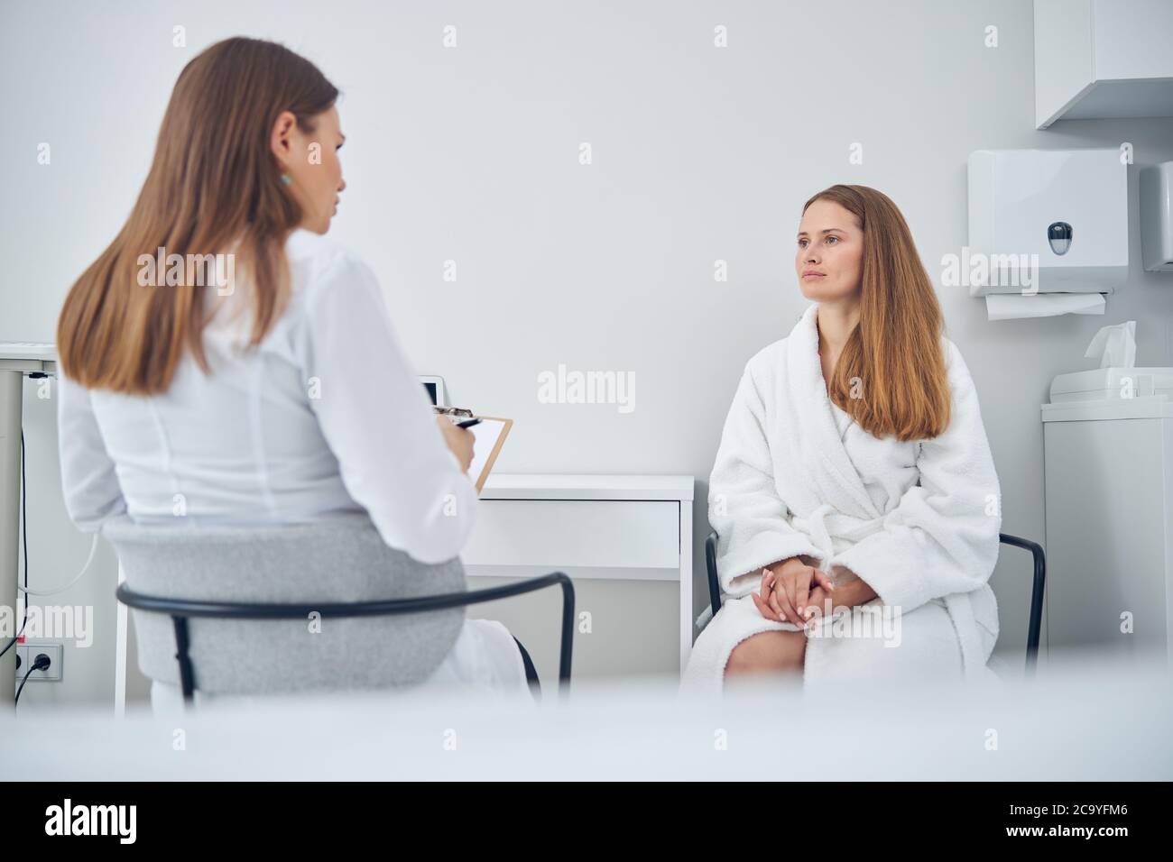 Ladies in white robes sitting on the chairs while having conversation ...