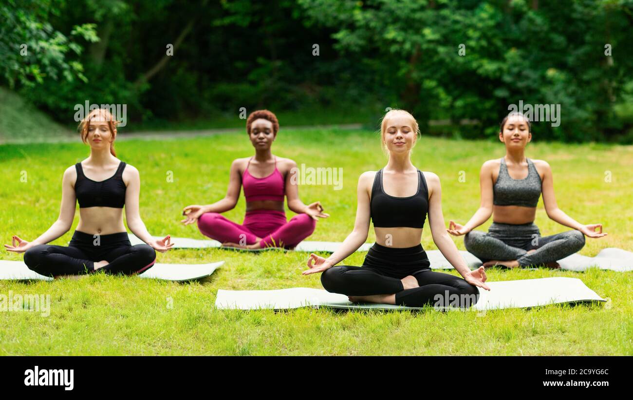 Outdoor yoga class. Group of diverse girls doing breathing exercises or