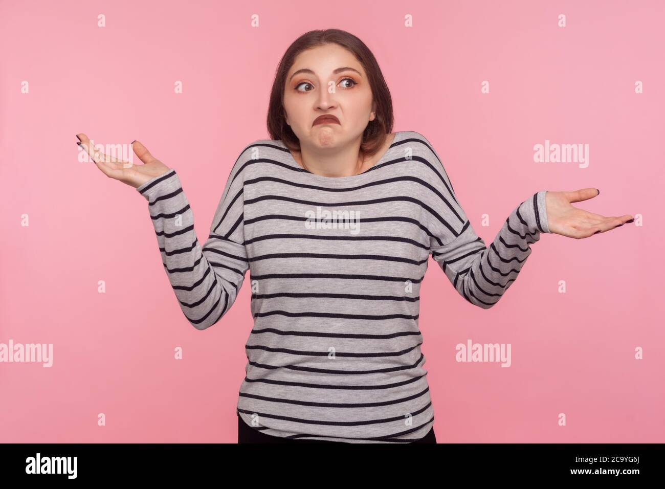 Don't know, whatever! Portrait of confused woman in striped sweatshirt shrugging shoulders in doubts, not sure and uncertain about difficult question. Stock Photo