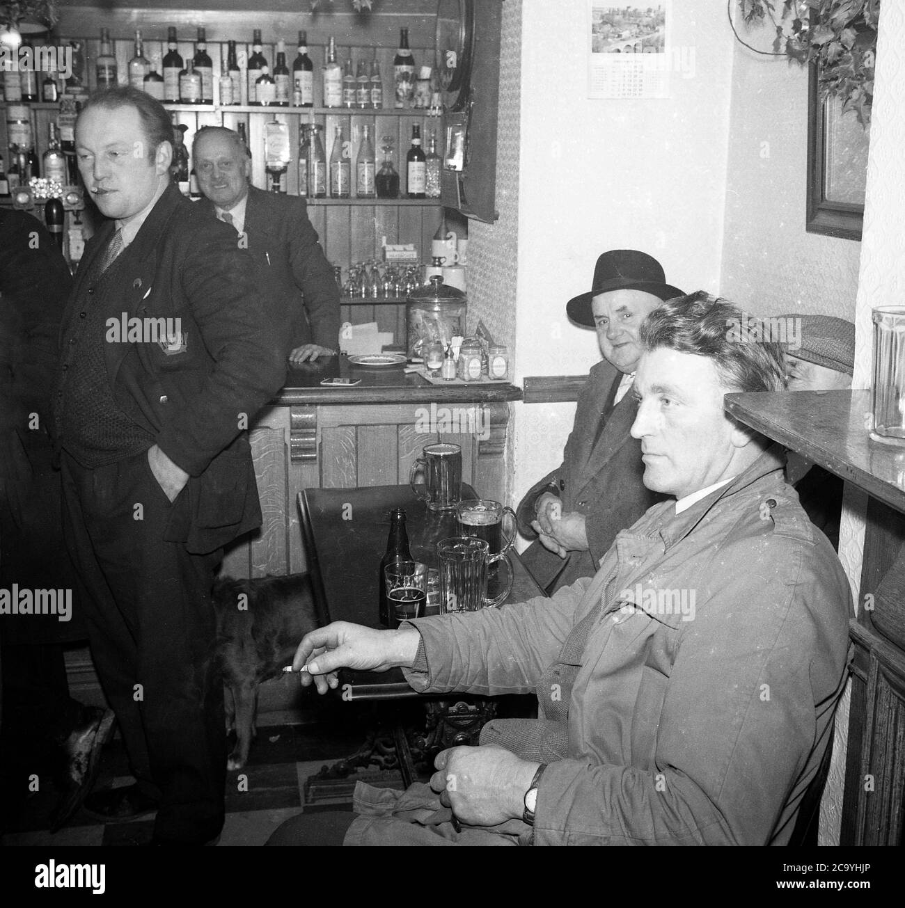 1950s, historical, three men, two sitting at a table, having a pint of beer or ale and a smoke at a bar in a pub after work, England, UK. Stock Photo