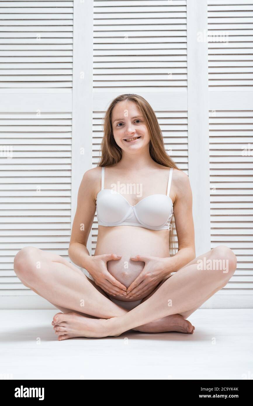 Beautiful young pregnant woman sitting on floor in Lotus position and smiling. Vertical frame. Stock Photo