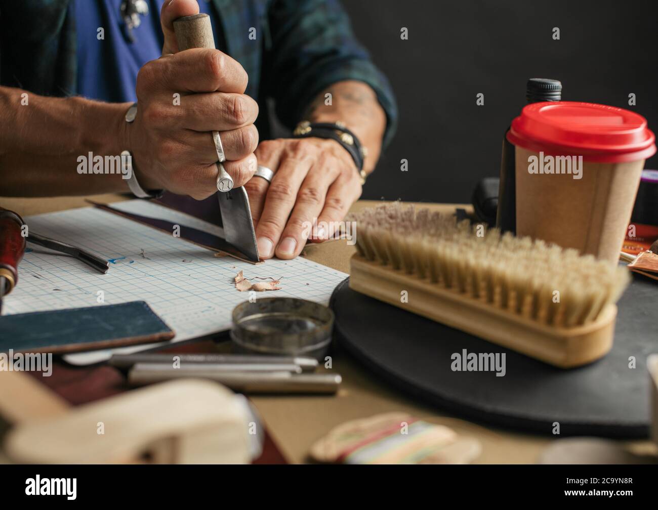 Leather goods master hands cutting piece of natural leather with crafting tool. Workflow in the workshop. Workflow in the workshop, close-up. Stock Photo