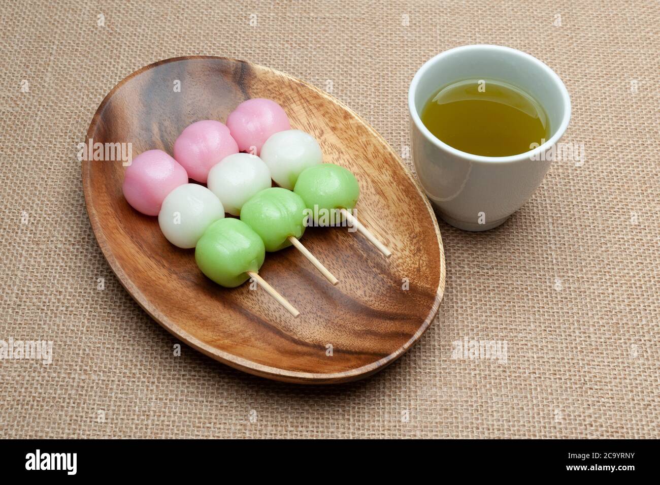 Japanese traditional sweet called Dango Mochi on wooden platter with green tea. Isolated on jute background. Close-up. Top view. Stock Photo